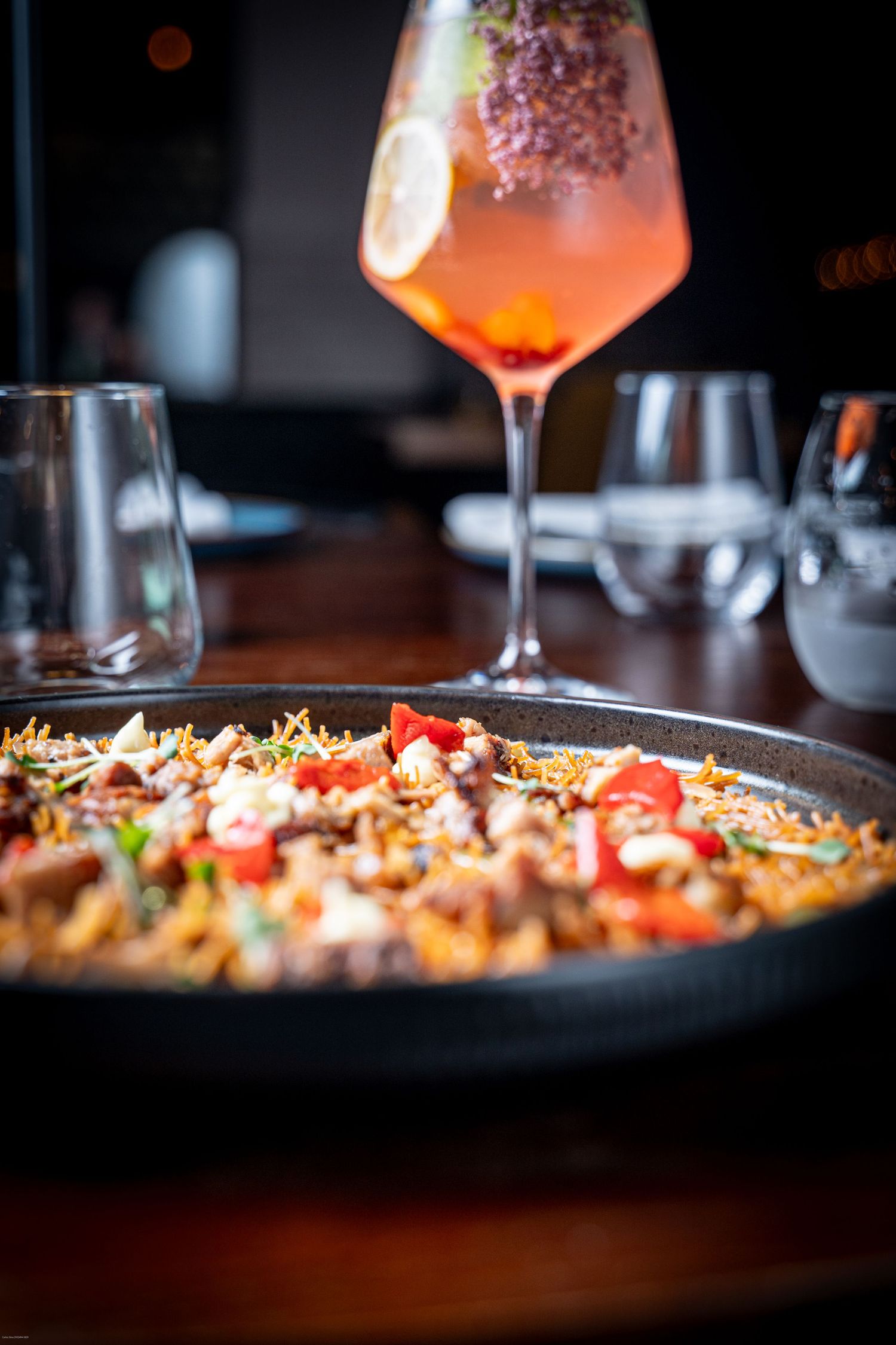 Close-up shot of cocktails and appetizers on a dark wooden table in a dimly lit restaurant setting.