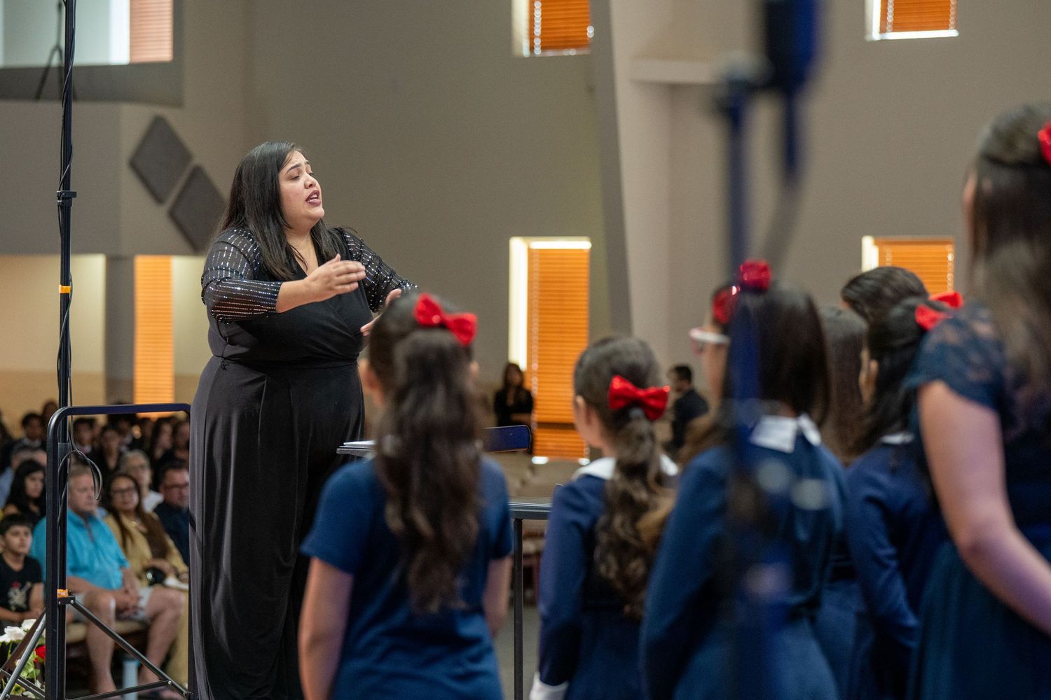 A conductor leads a group of young students in graduation gowns and caps during a school ceremony.