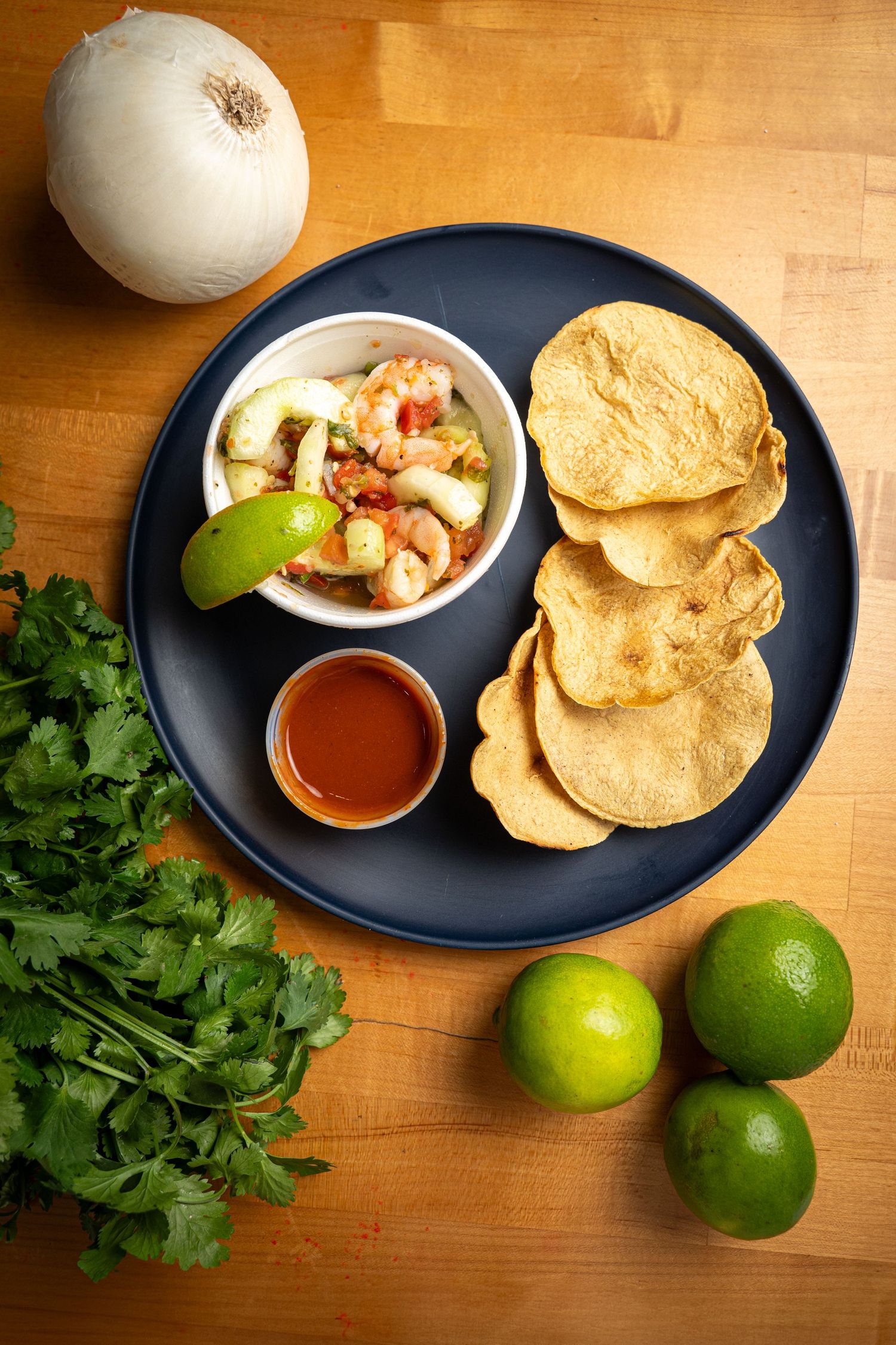 Fresh Mexican appetizer plate with shrimp ceviche, tortilla chips, hot sauce, limes, onion and cilantro on wooden table.