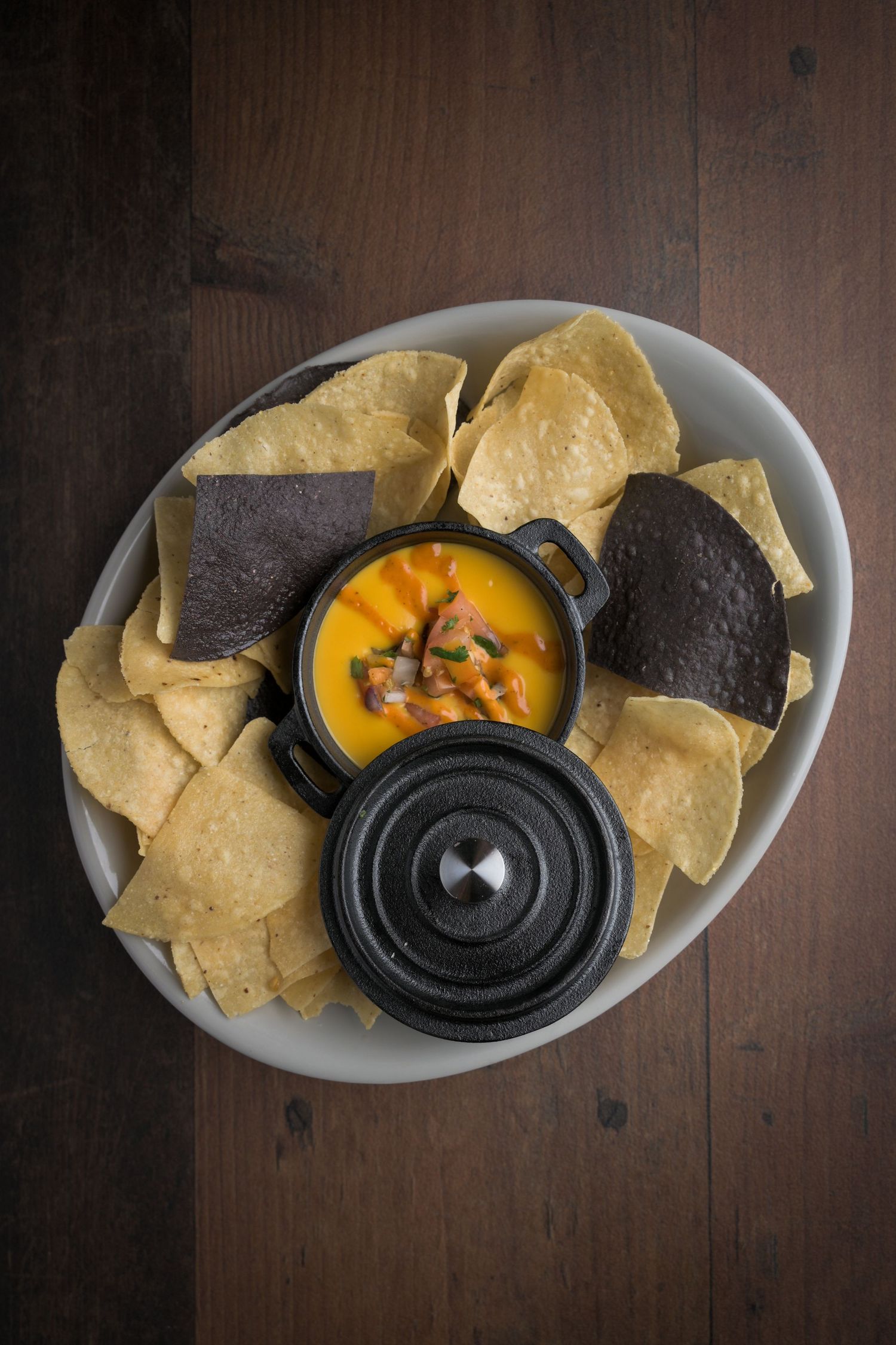 Tortilla chips served with melted queso dip in a black cast iron pot.