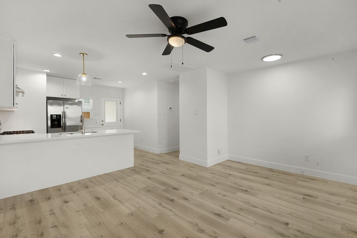 Large open concept living space with ceiling fans, recessed lighting, and light wood flooring throughout.