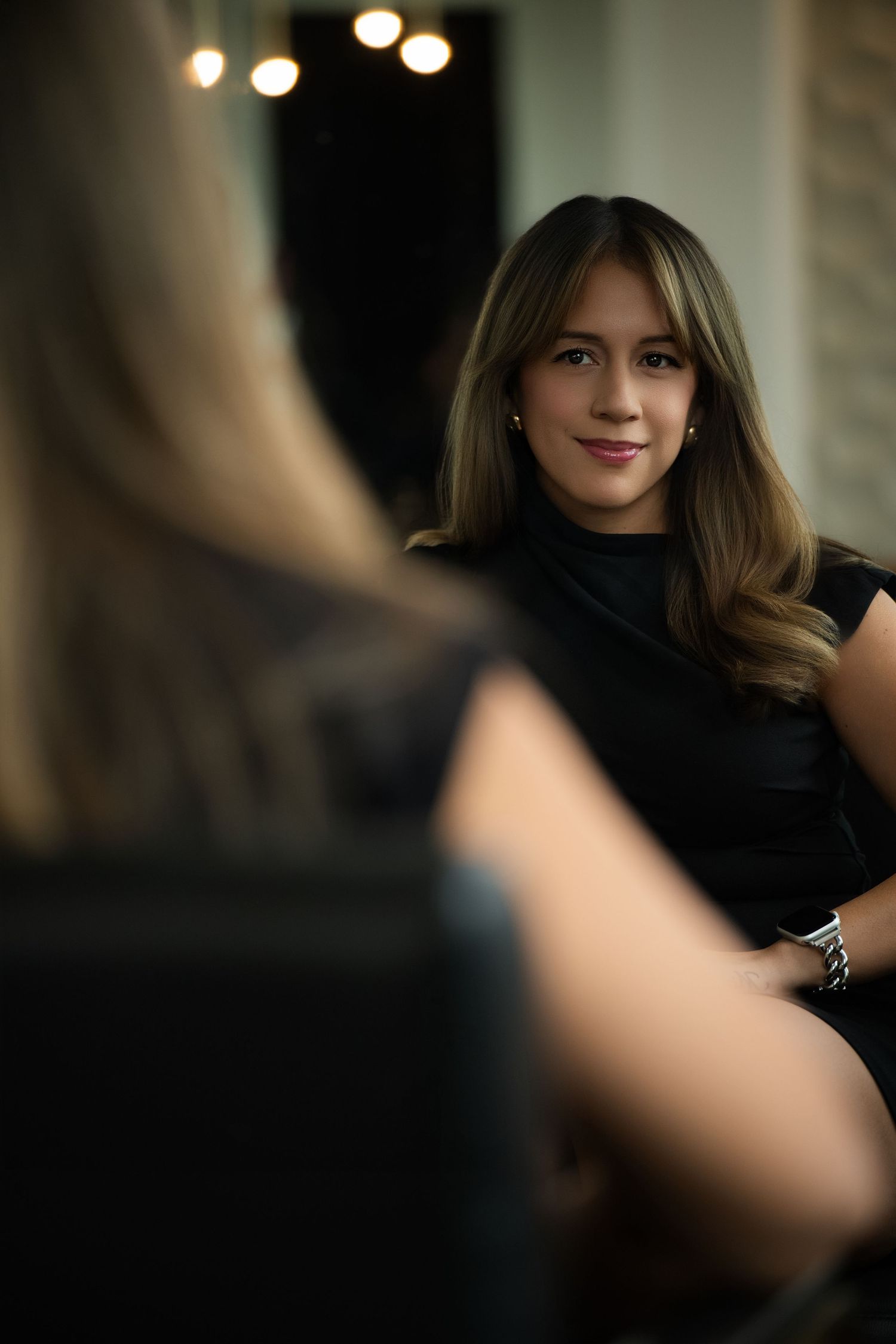 Elegant portrait of someone in a black outfit sitting with soft lighting and bokeh effects.