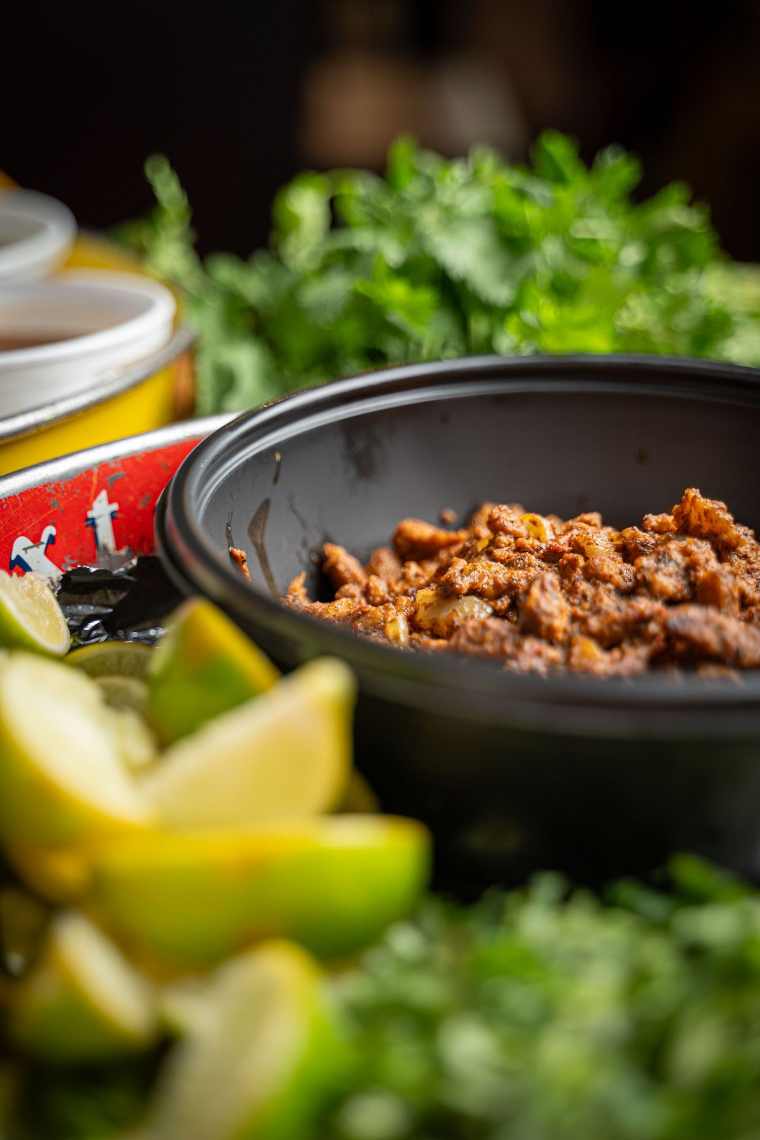 Bowl of seasoned ground meat filling garnished with fresh herbs and citrus wedges for tacos.