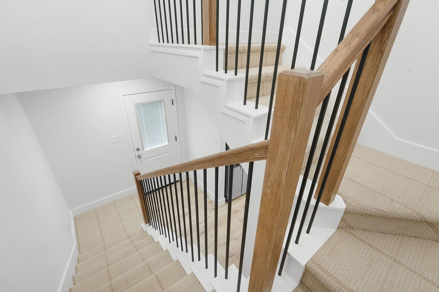 White staircase with wooden handrails and black metal balusters in a contemporary home interior.