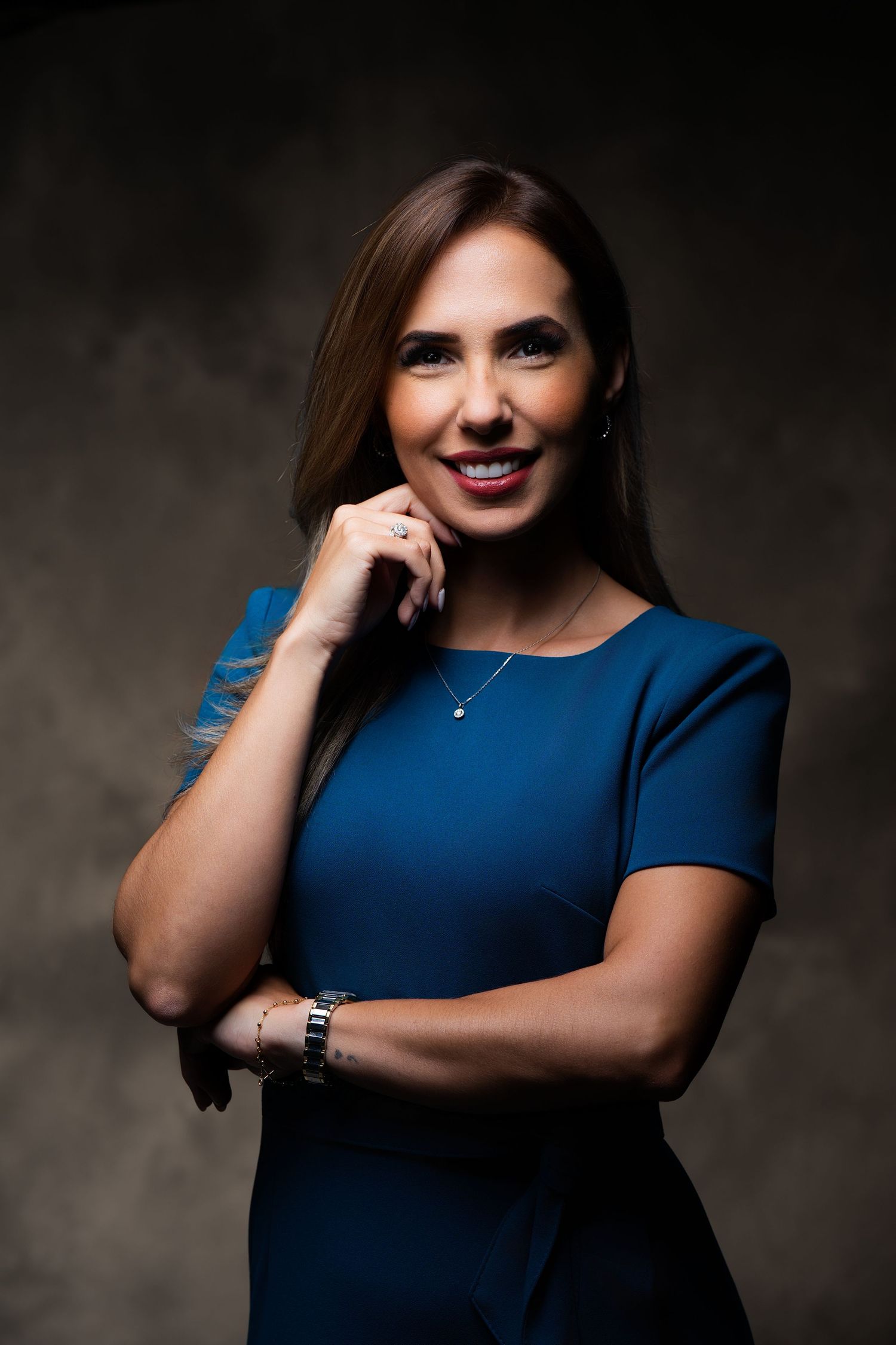Professional studio portrait of someone in a royal blue dress smiling against a dark background.