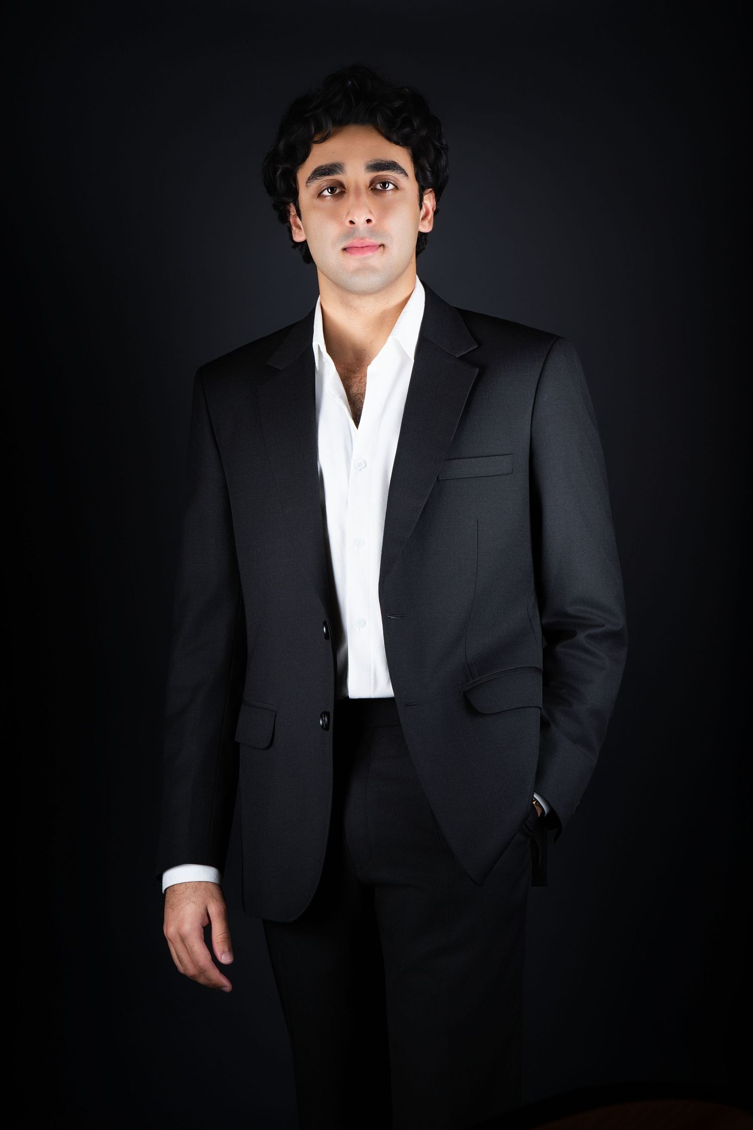 Professional studio portrait of someone wearing a black suit and white dress shirt against a dark background.