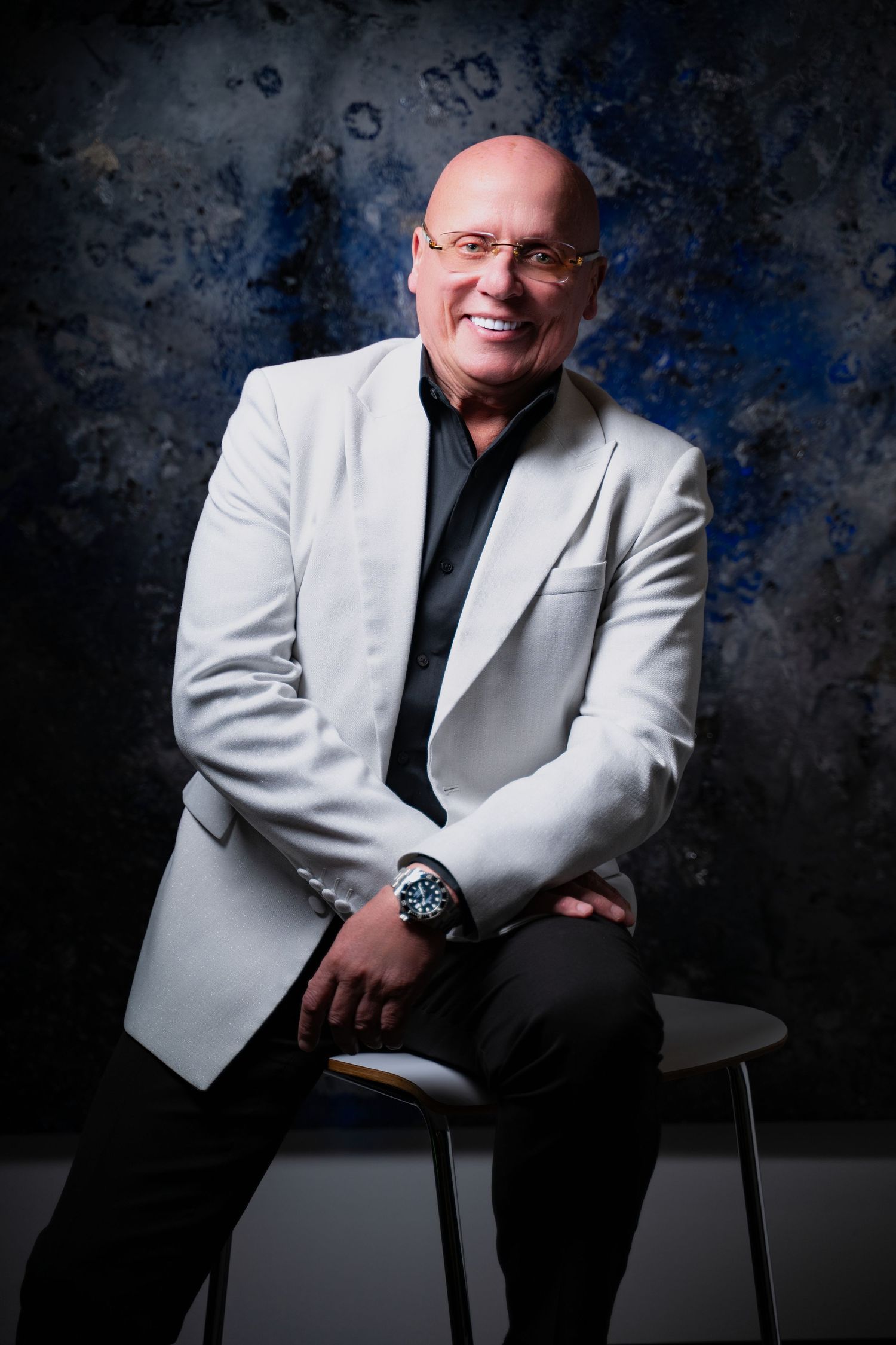 Studio portrait of person in white blazer against textured blue backdrop.