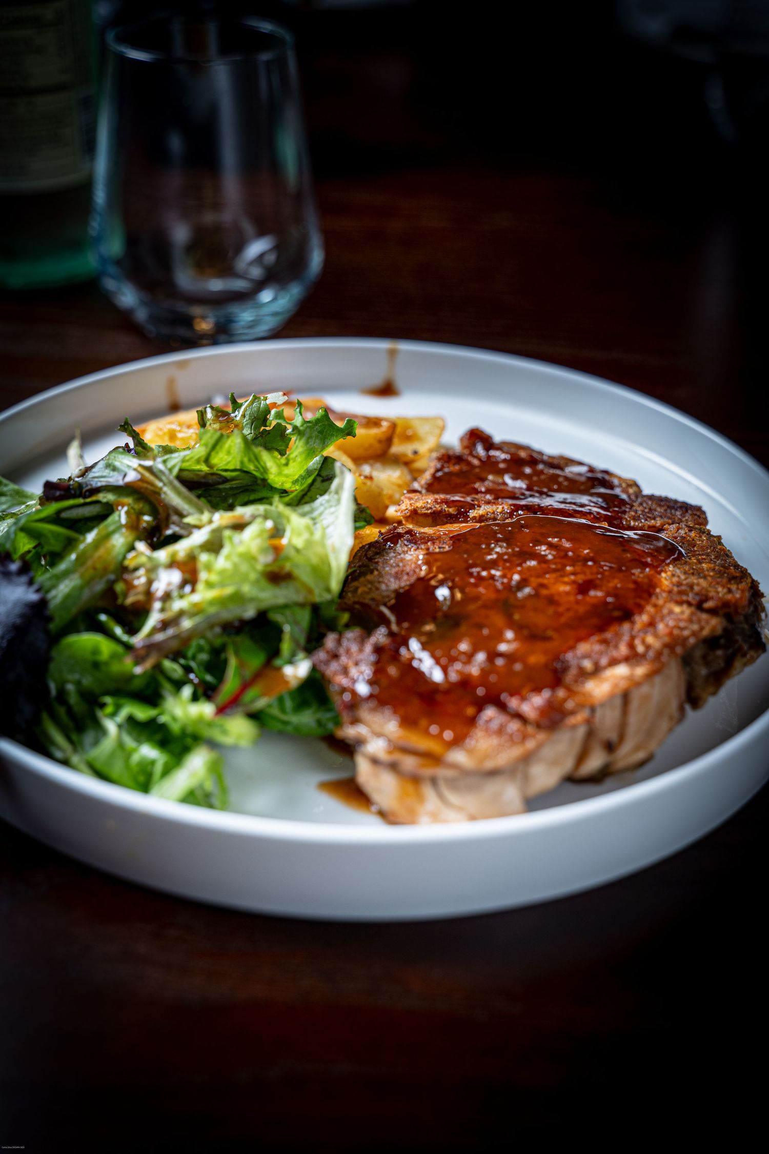 A series of plated glazed salmon fillets with fresh green salad served on white dishes in moody lighting.
