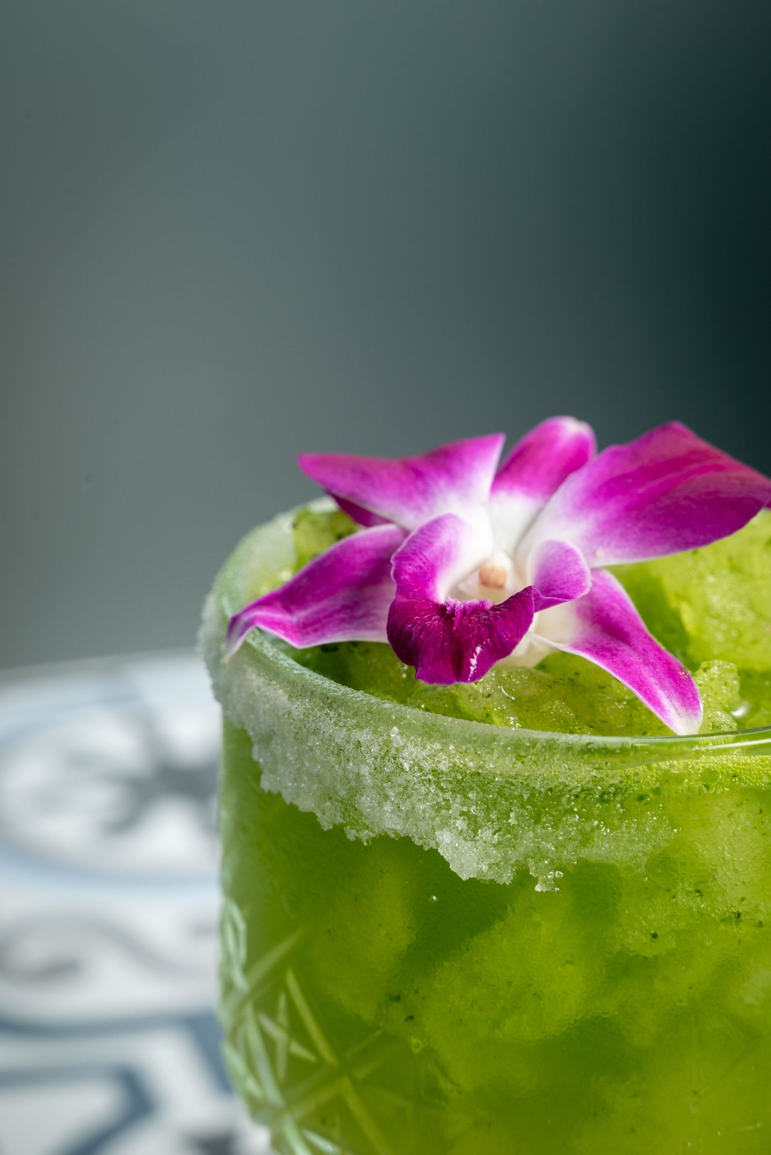 Green tropical cocktail garnished with vibrant purple orchid flower and crushed ice.