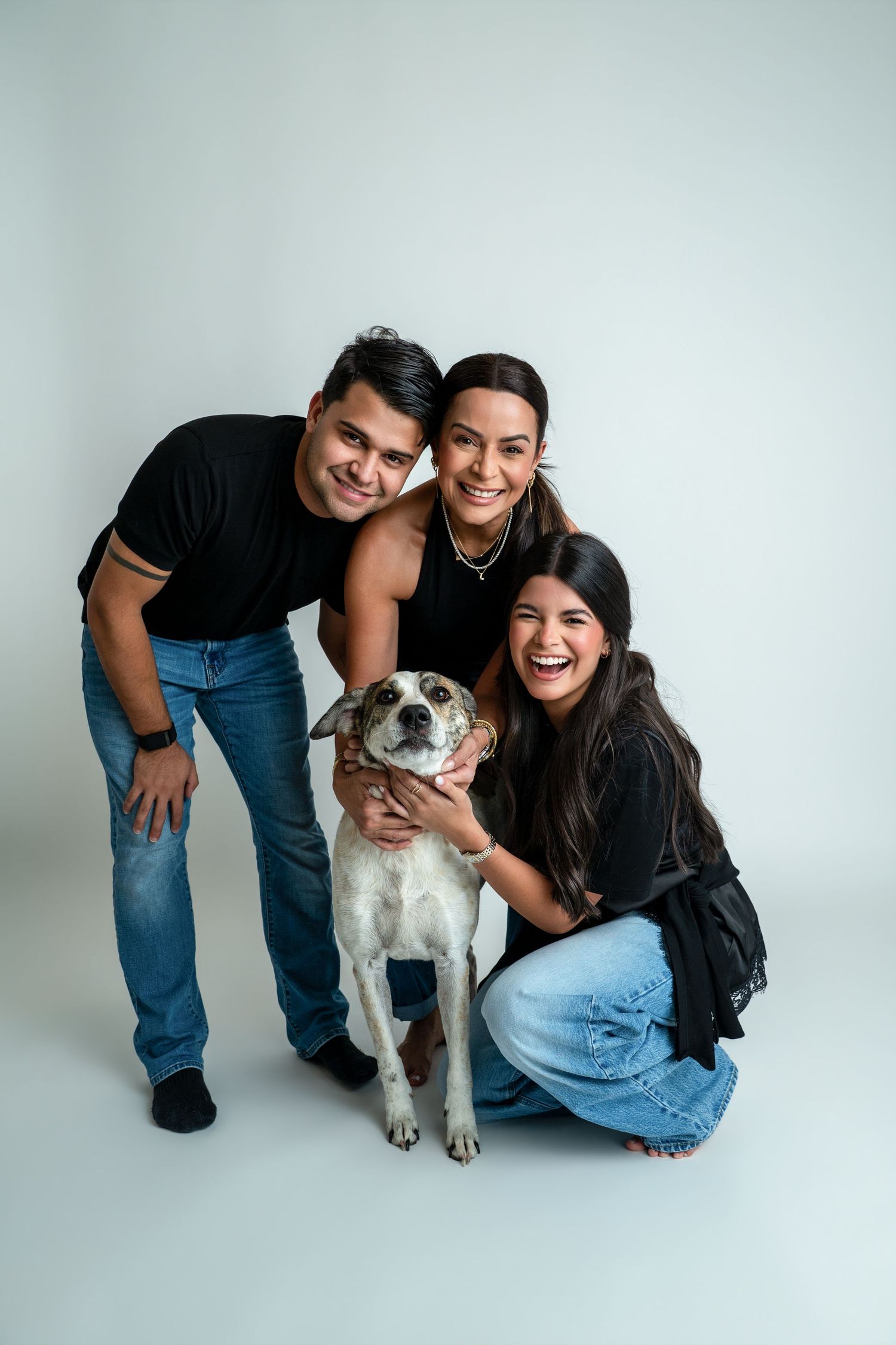 Happy family of two women and a man posing with their brown and white dog in a studio photo.