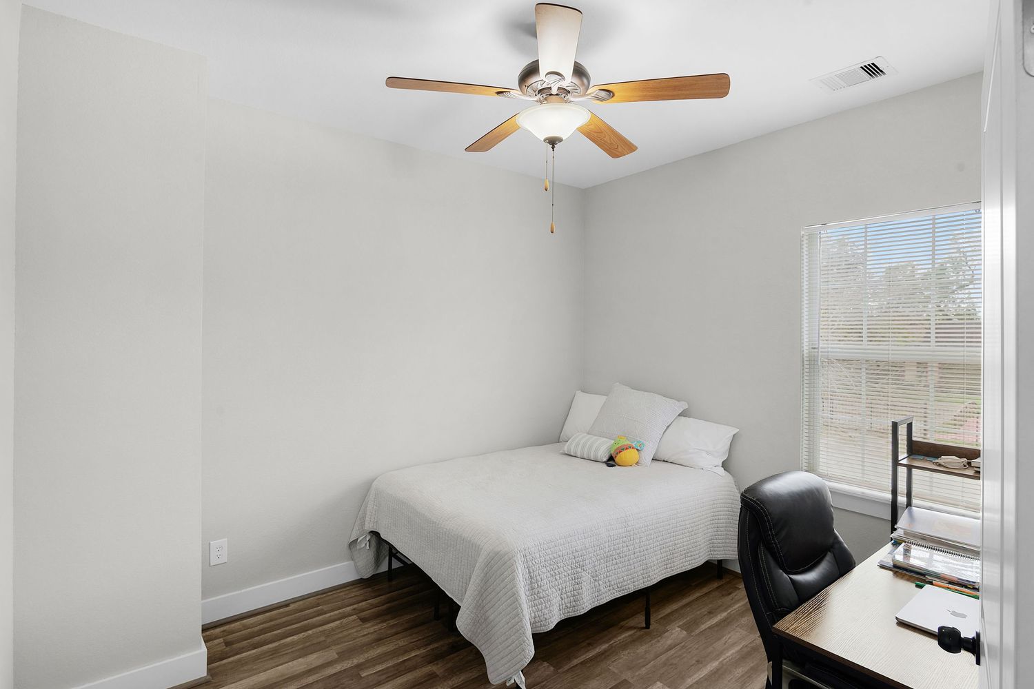 Minimalist bedroom with white bedding, ceiling fan, and large window offering natural light.