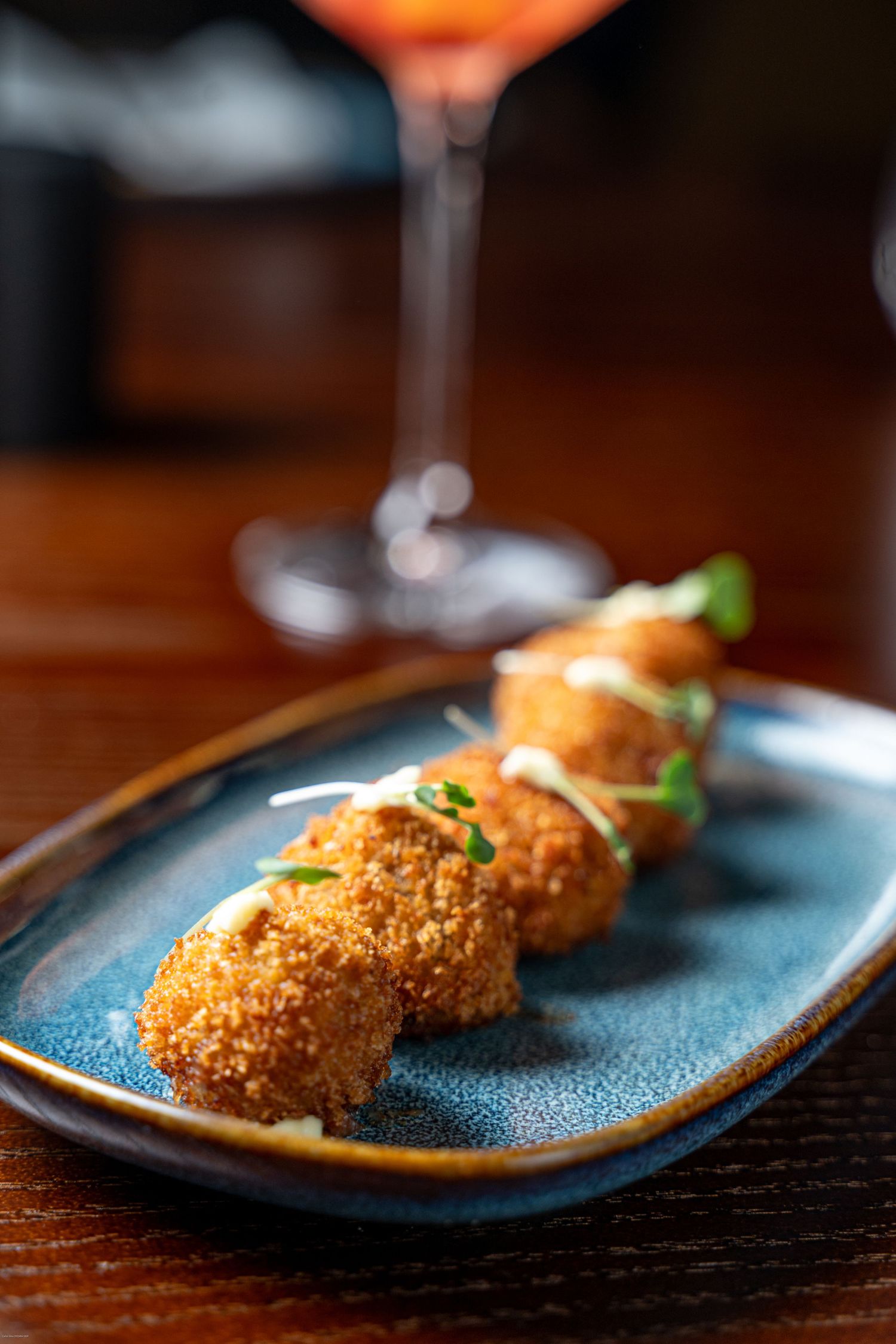Crispy breaded appetizers on a blue ceramic plate with cocktail glass in background.