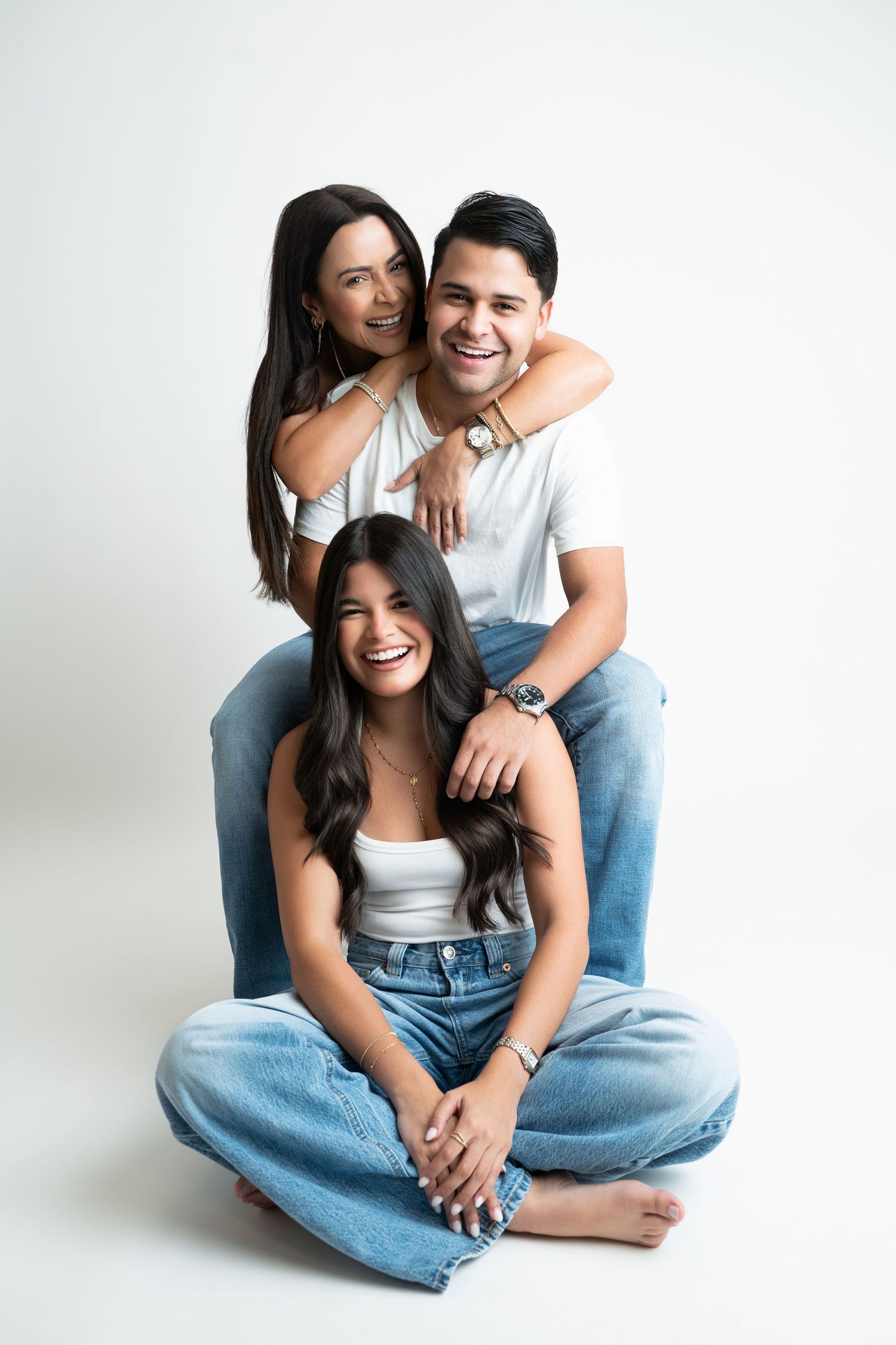 Three smiling people in white tops and jeans pose together in a bright studio portrait photo.