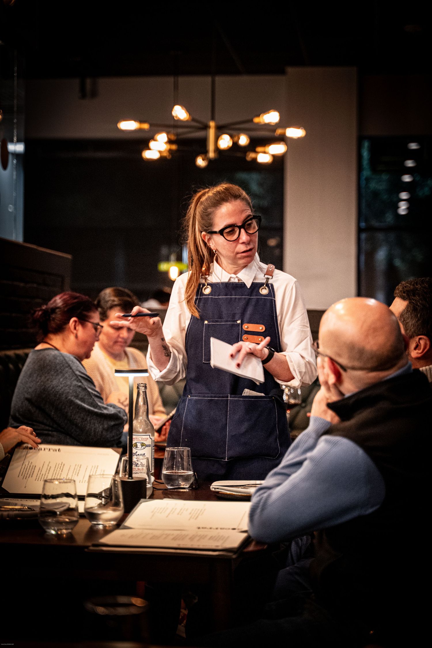 Restaurant staff interacting with diners at a dimly lit table during dinner service.