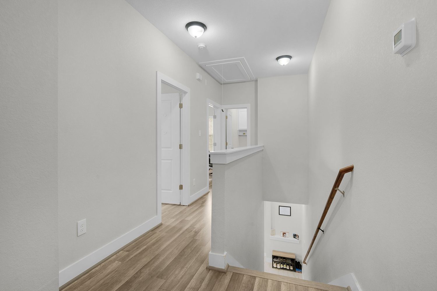 White hallway with recessed lighting and wooden flooring leading to multiple doorways.