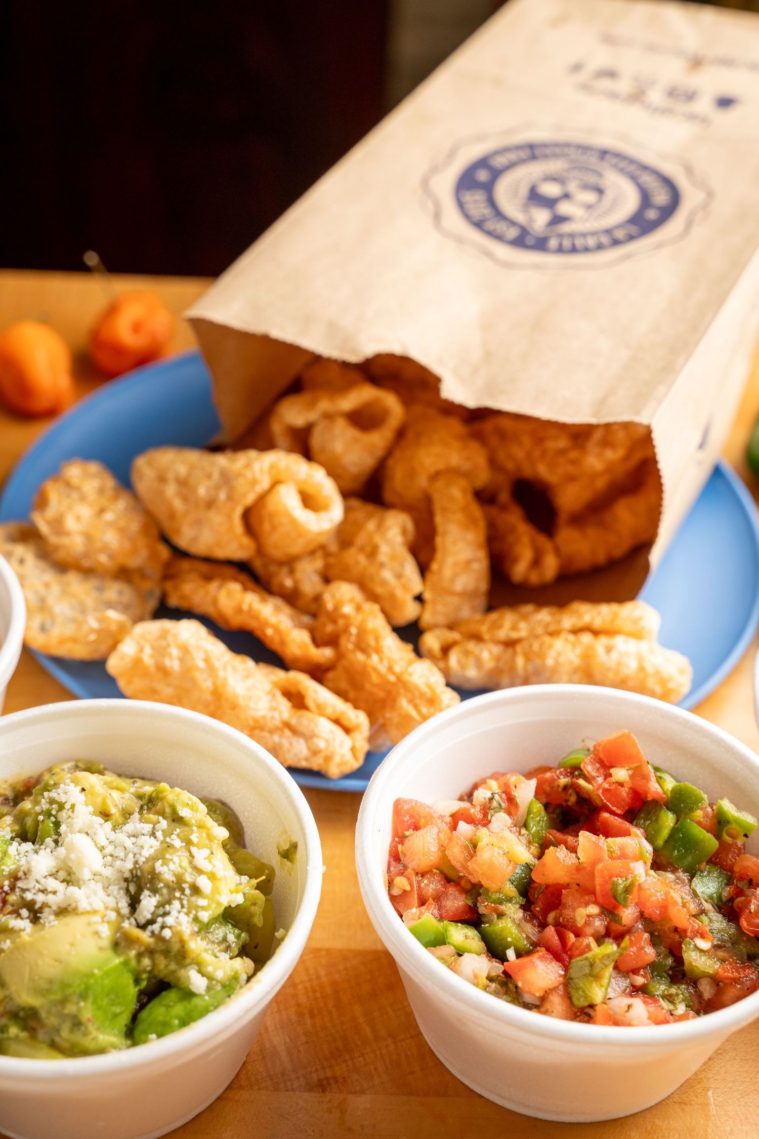 Fresh guacamole, pico de gallo, and queso dips served with crispy tortilla chips in white bowls on wooden surface.