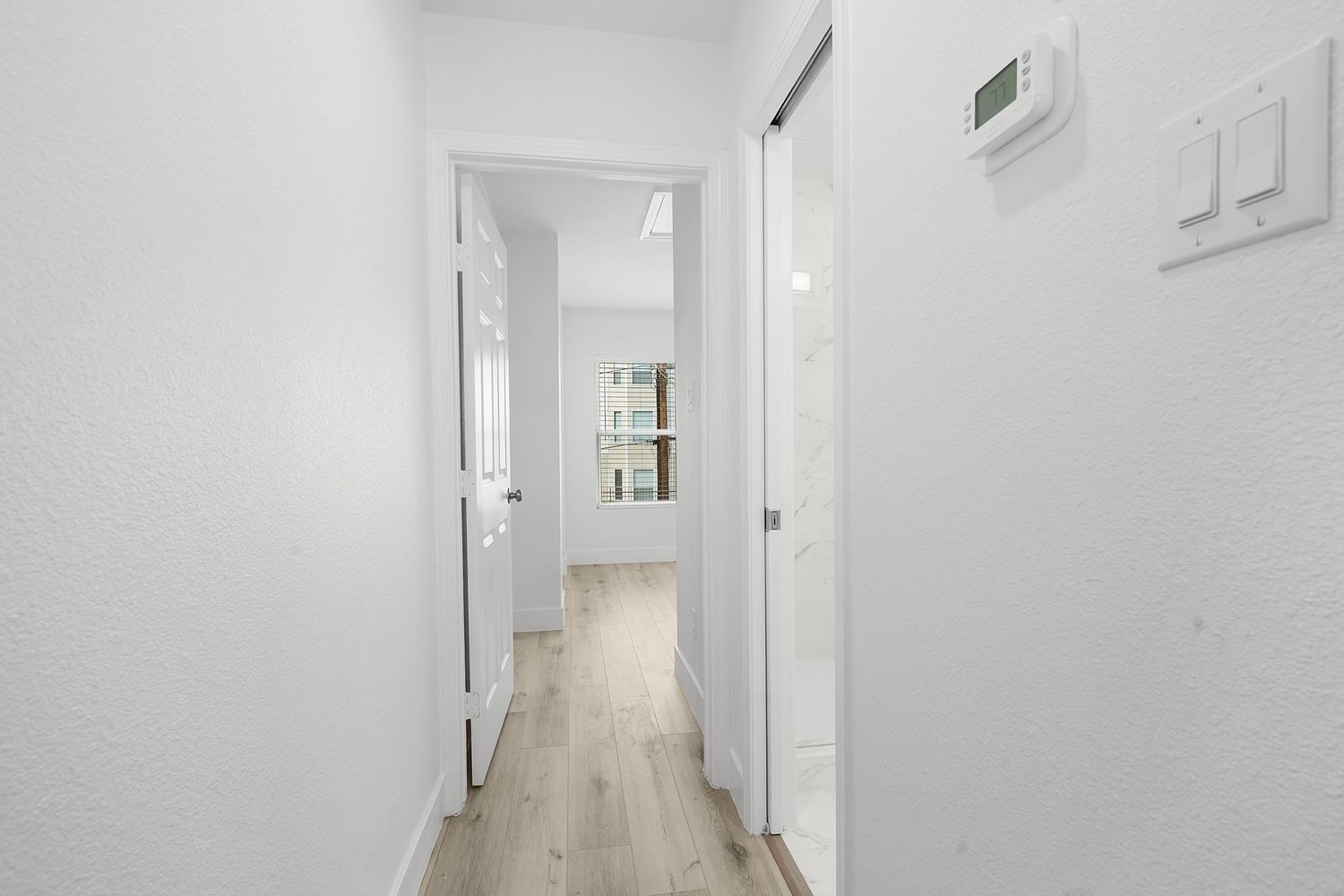 Modern white hallway with hardwood floors, recessed lighting and minimalist design features a sleek contemporary aesthetic.