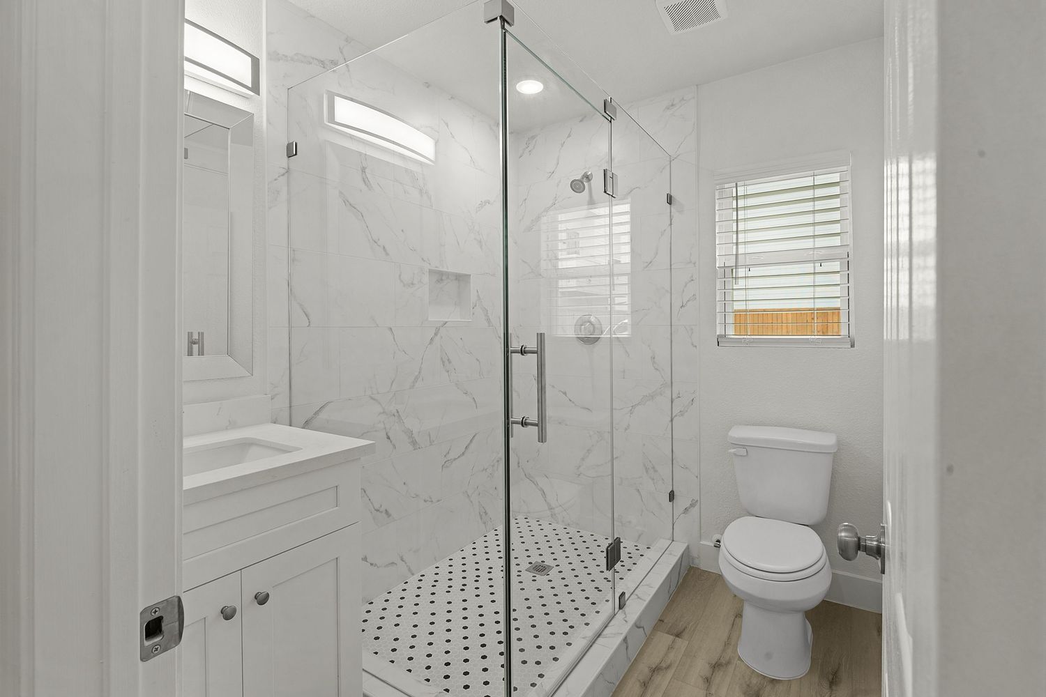 Modern bathroom with marble-look tile, glass shower enclosure and white vanity.