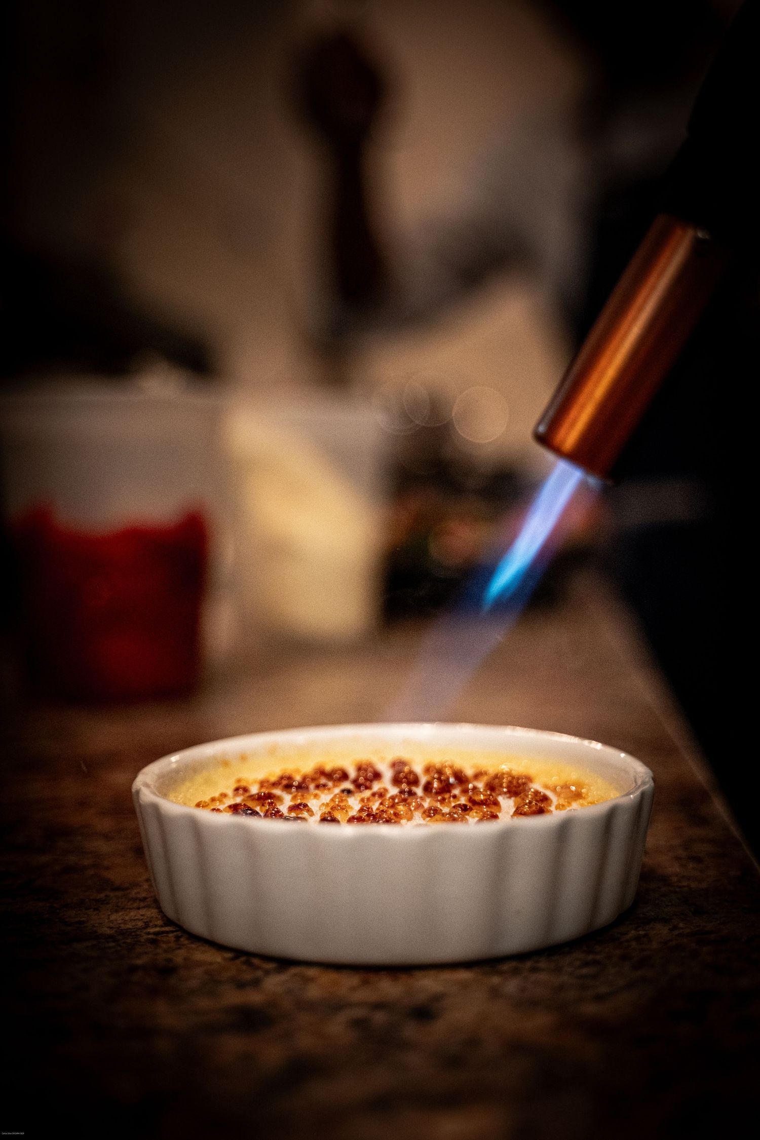 Sequence showing kitchen torch browning and caramelizing the top of a dessert in a white ceramic dish.