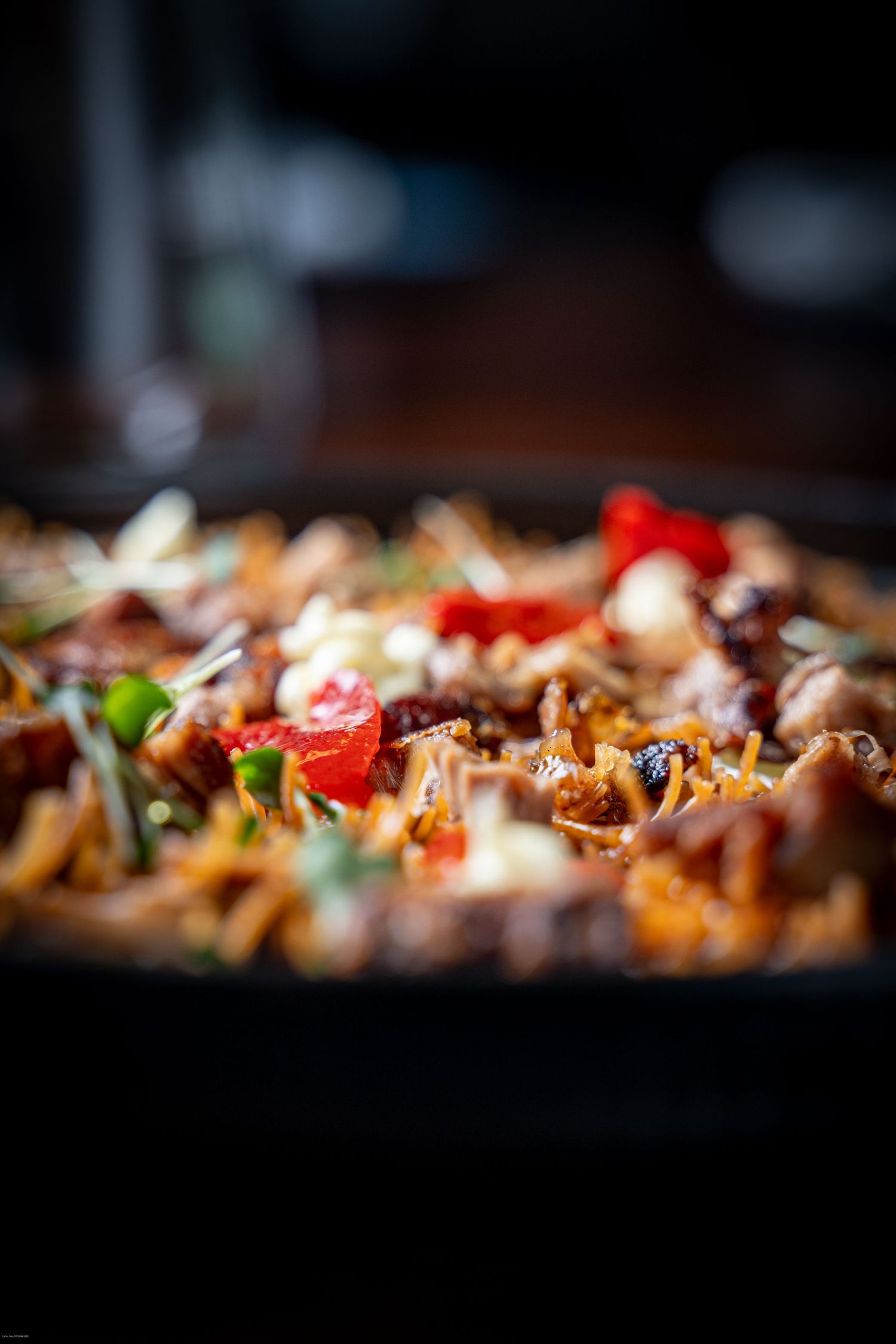 Close-up of sizzling stir fry with colorful vegetables and meat in a dark pan with selective focus.