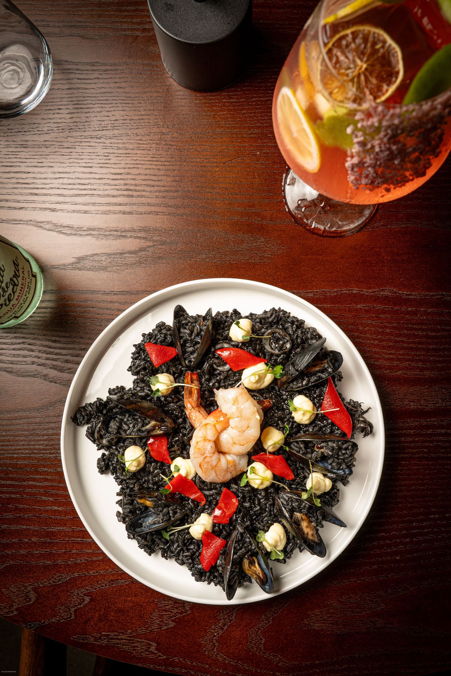 Black squid ink seafood dish with shrimp, red peppers and light garnishes on white oval plates.
