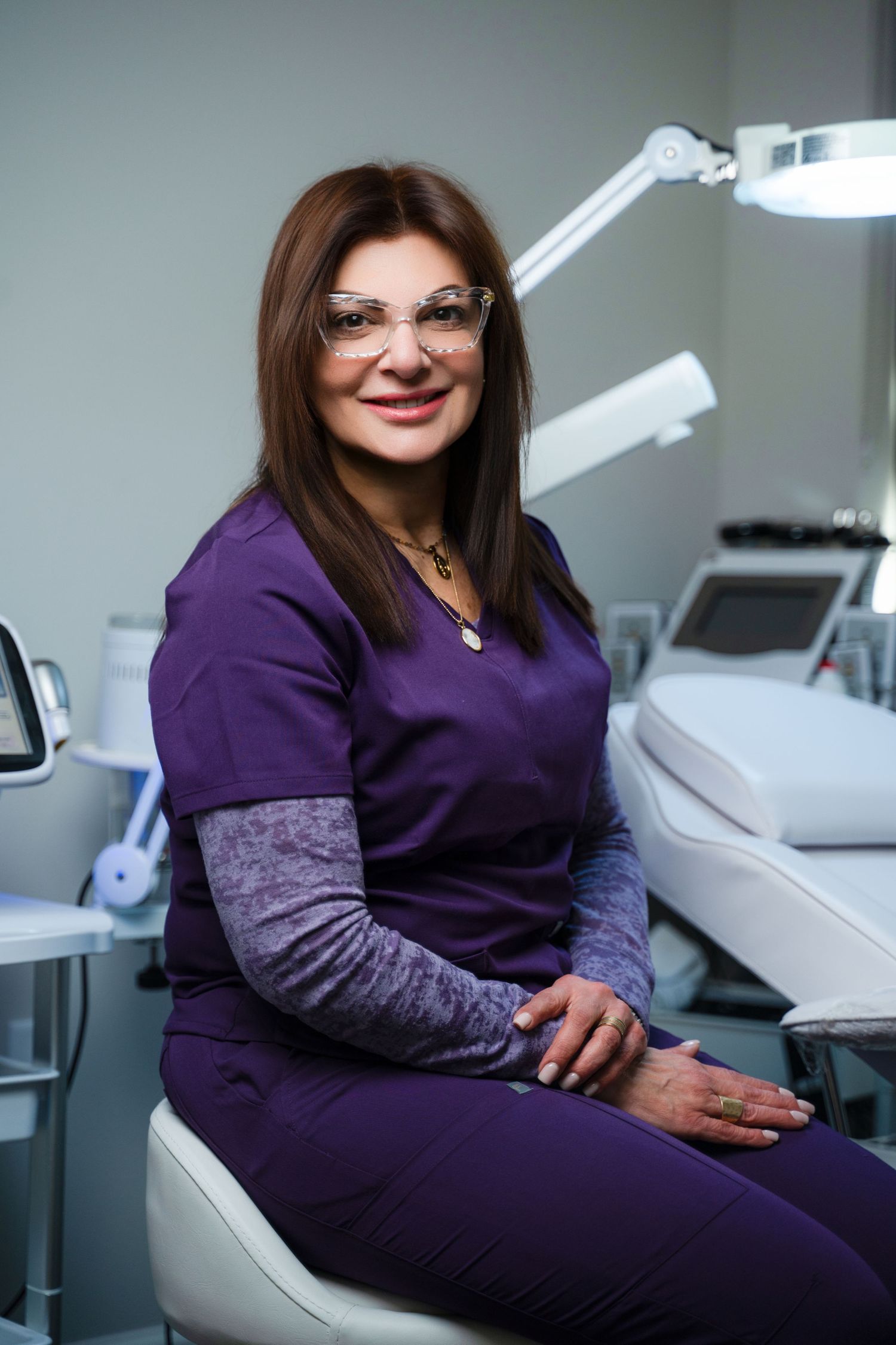 Healthcare professional in purple scrubs sits in dental office chair with modern medical equipment visible in background.