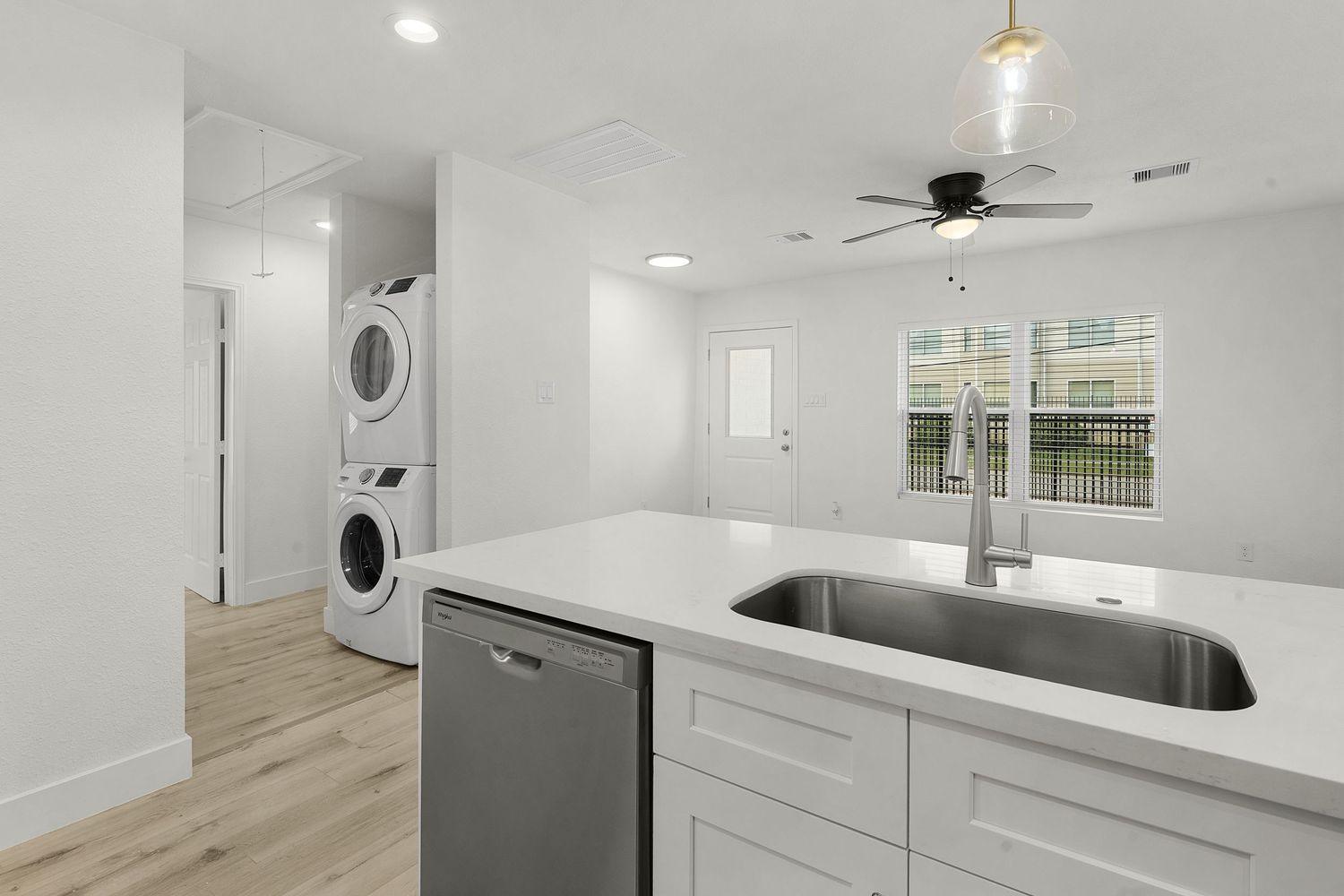 Modern laundry room with stacked washer/dryer, white cabinets and stainless steel sink.