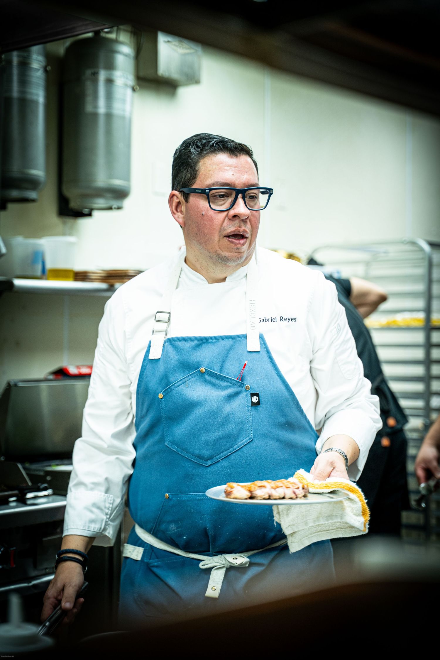 Chef in white coat and blue apron plates dishes in professional kitchen.
