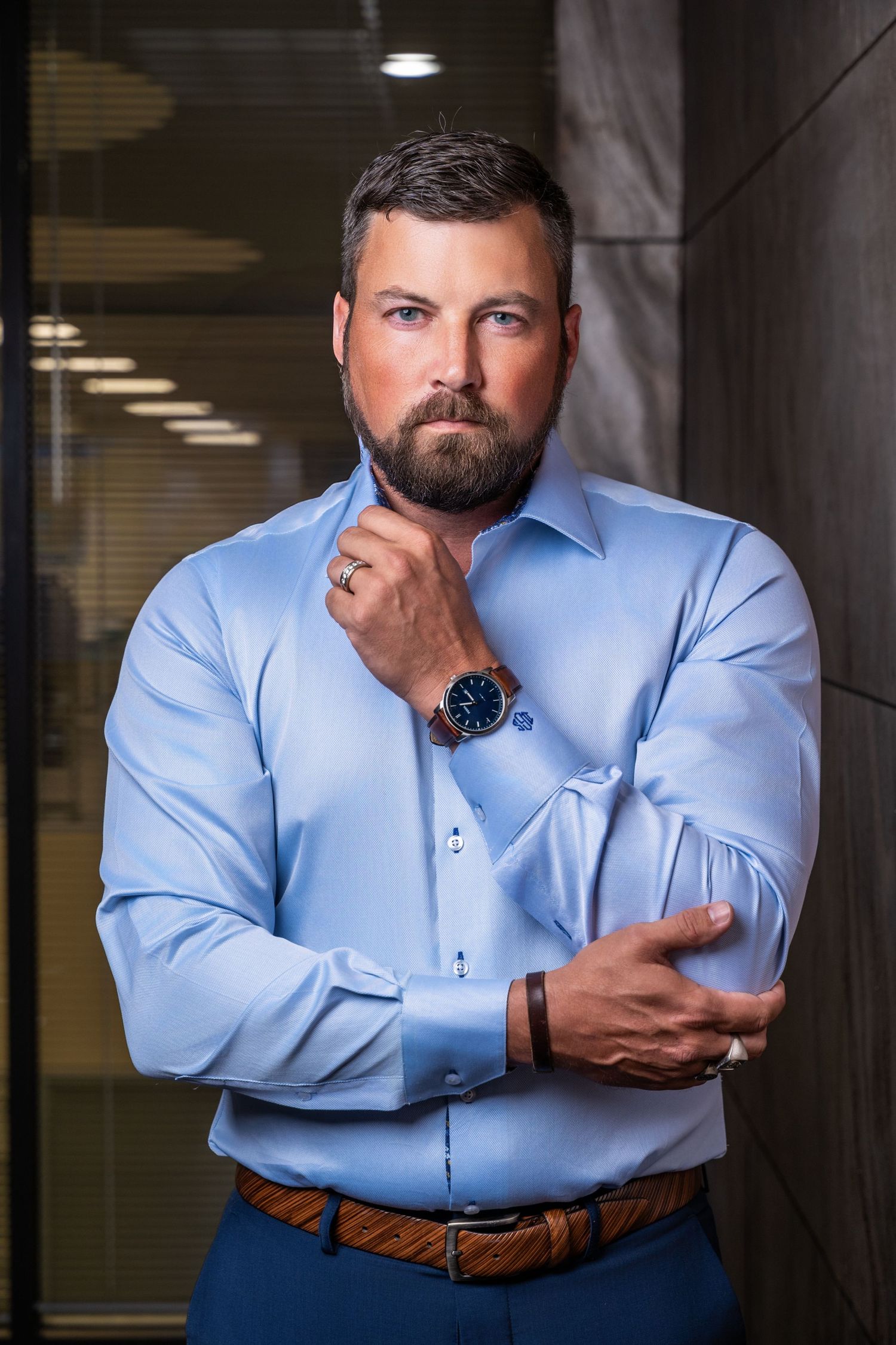 Corporate headshot series showing person in blue button-down shirt against grey wall.
