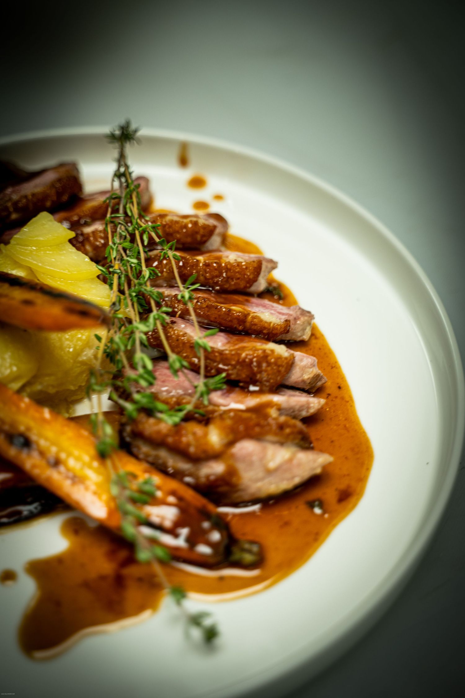 Sliced duck breast served with fresh thyme and rich sauce on white plate with roasted vegetables.