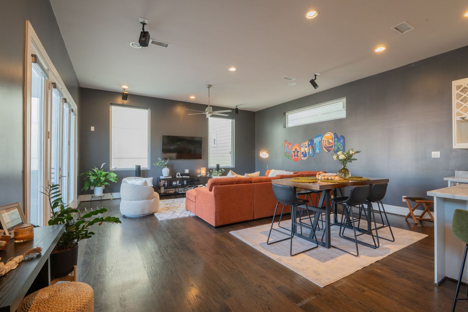 Modern open-concept living and dining area with dark hardwood floors, gray walls, orange sofa, and stylish bar seating.