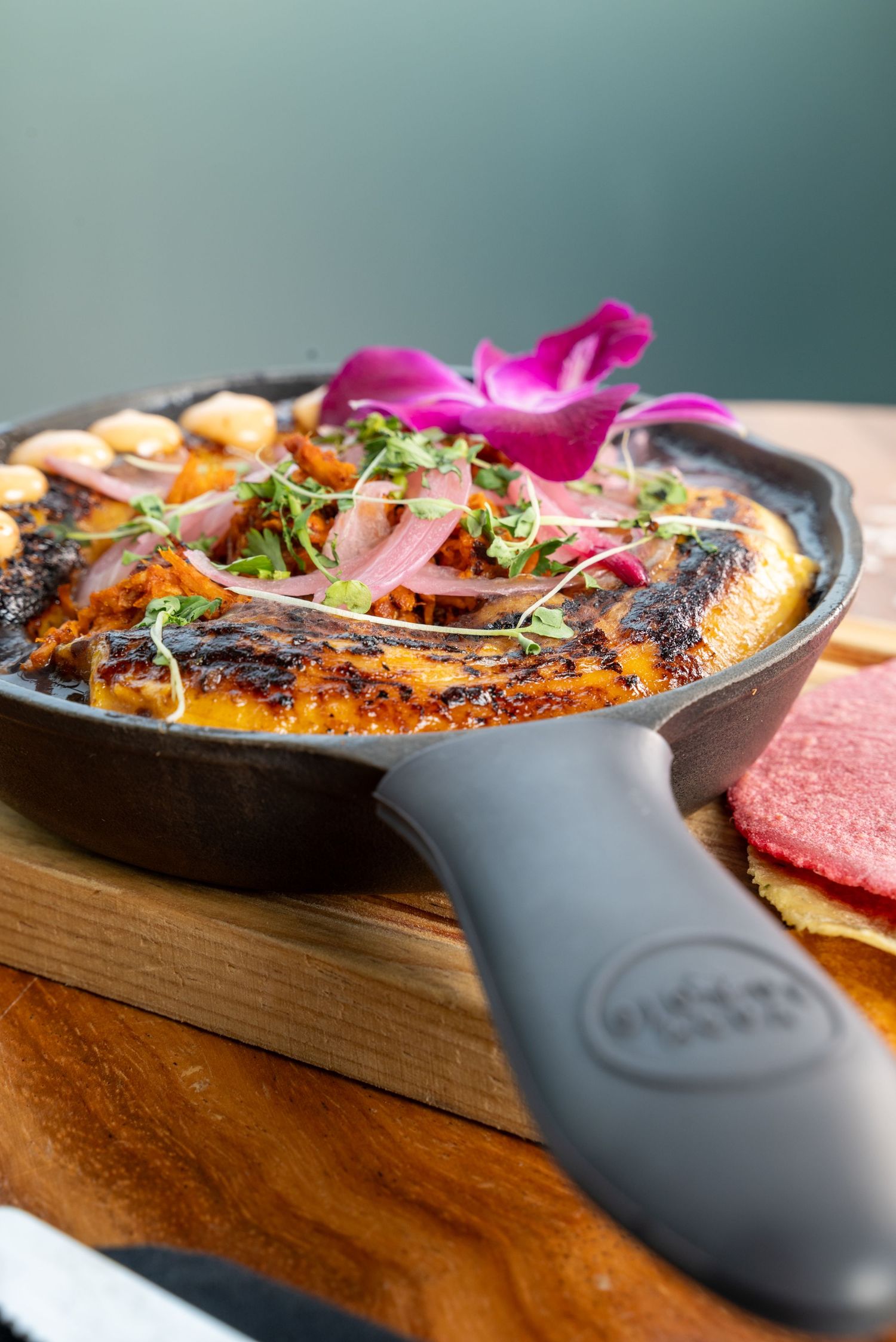 Garnished dish in cast iron skillet with pink flower petals and fresh herbs.