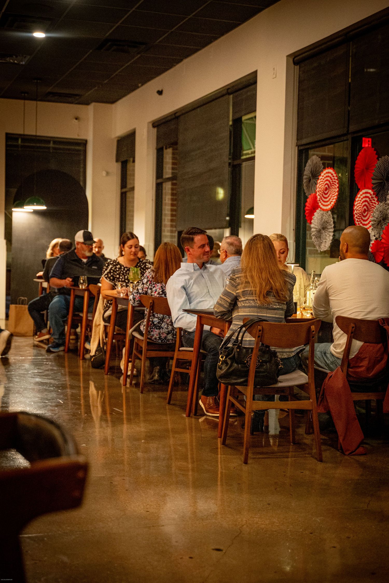 Diners enjoying a cozy evening at a restaurant with warm lighting and wooden chairs along a bar counter.
