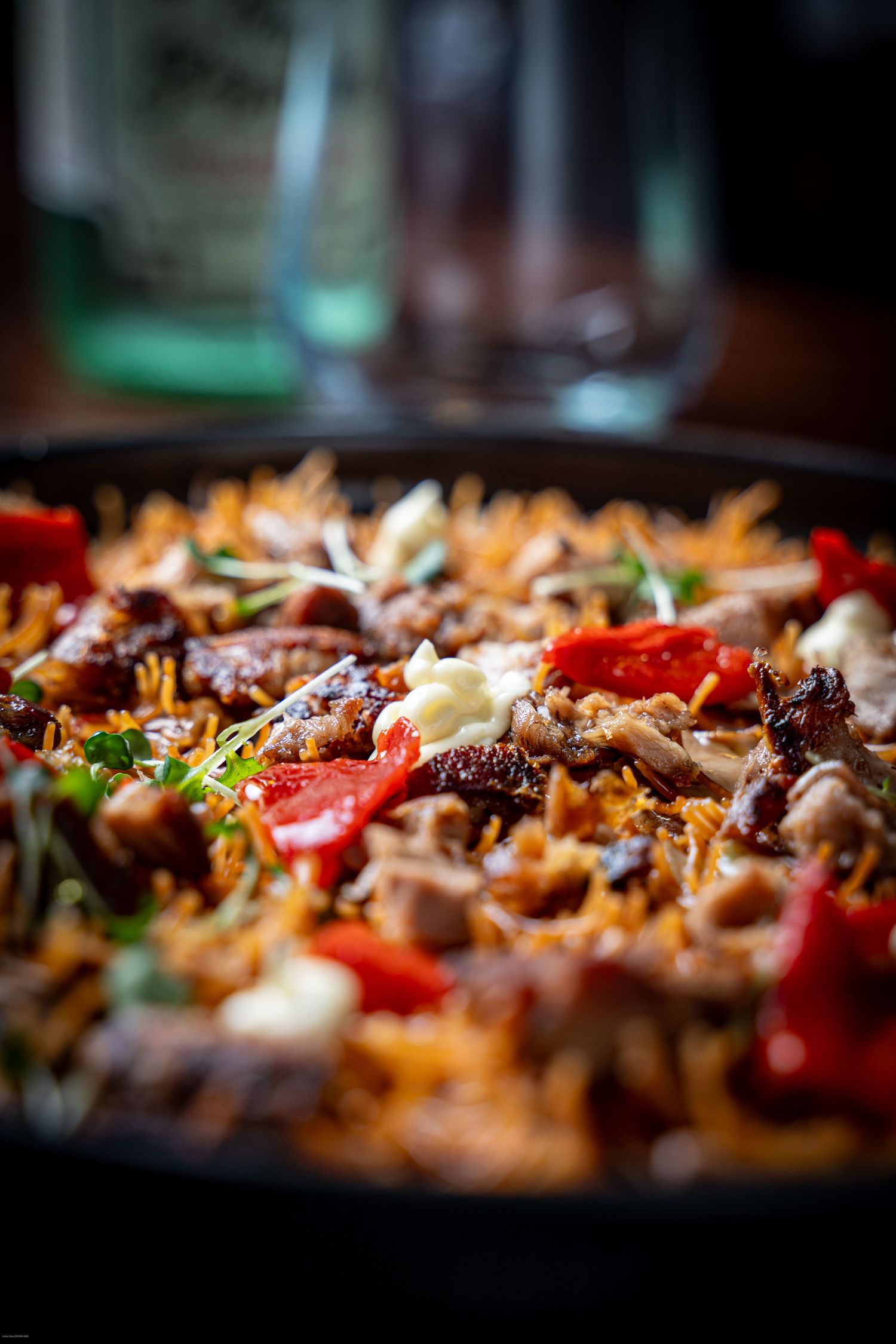 Close-up of colorful Mexican-style nachos loaded with melted cheese, tomatoes, meat and toppings in dark pan.
