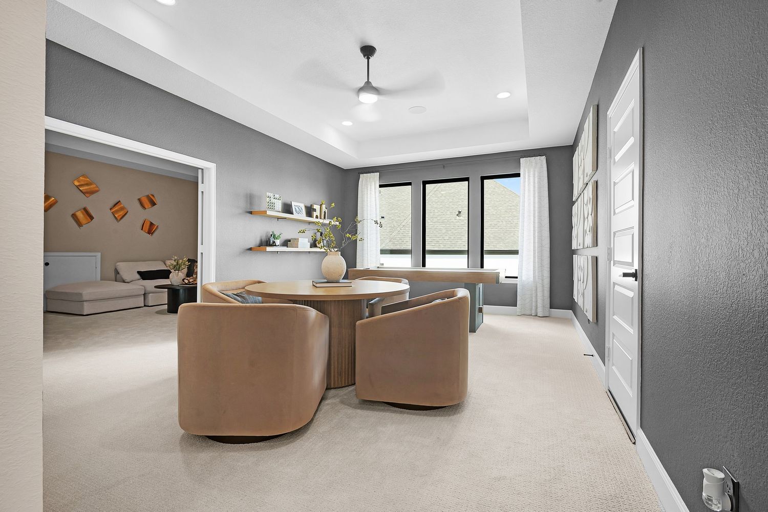 Contemporary living space with tan swivel chairs, floating shelves, and gray walls in an open floor plan.
