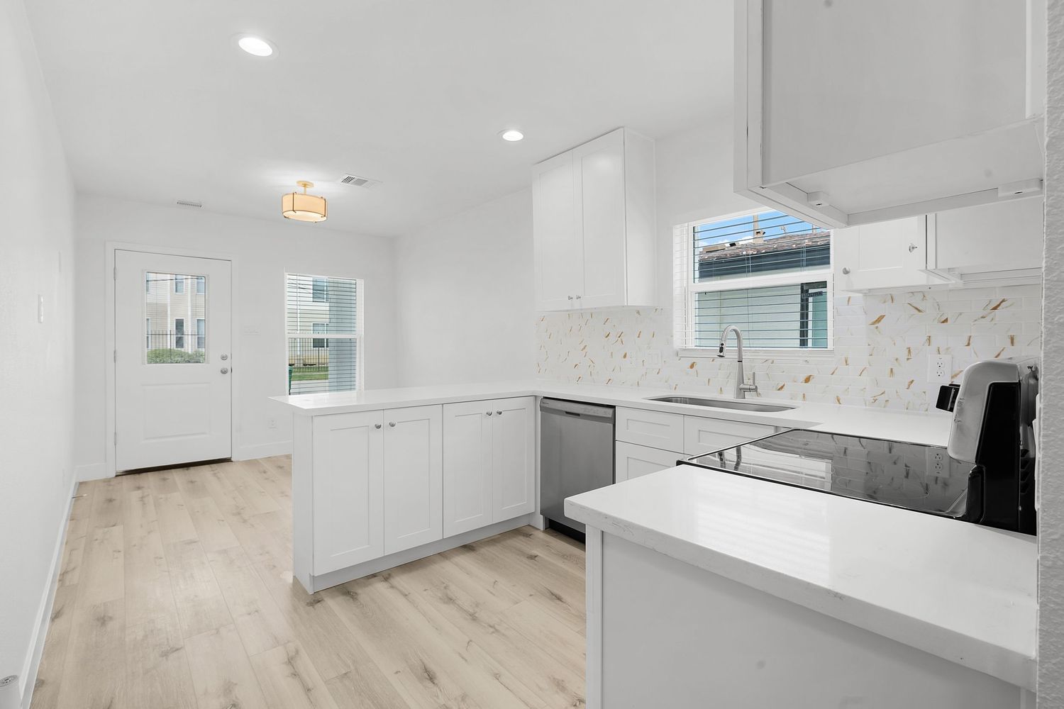Modern interior hallway with white walls, recessed lighting, and light wood flooring extending through multiple rooms.