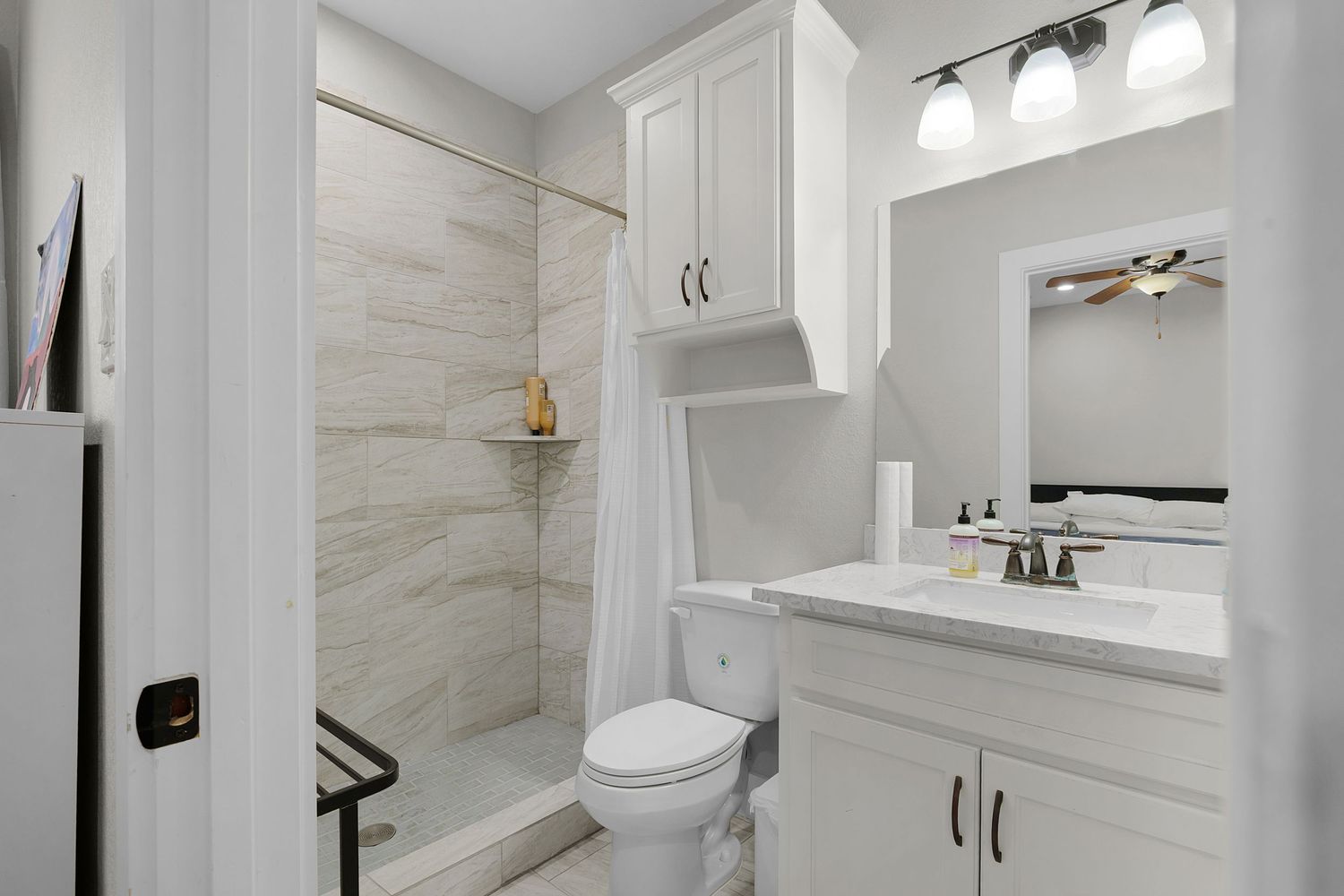 Elegant bathroom with marble-look shower, white vanity, and modern light fixtures.