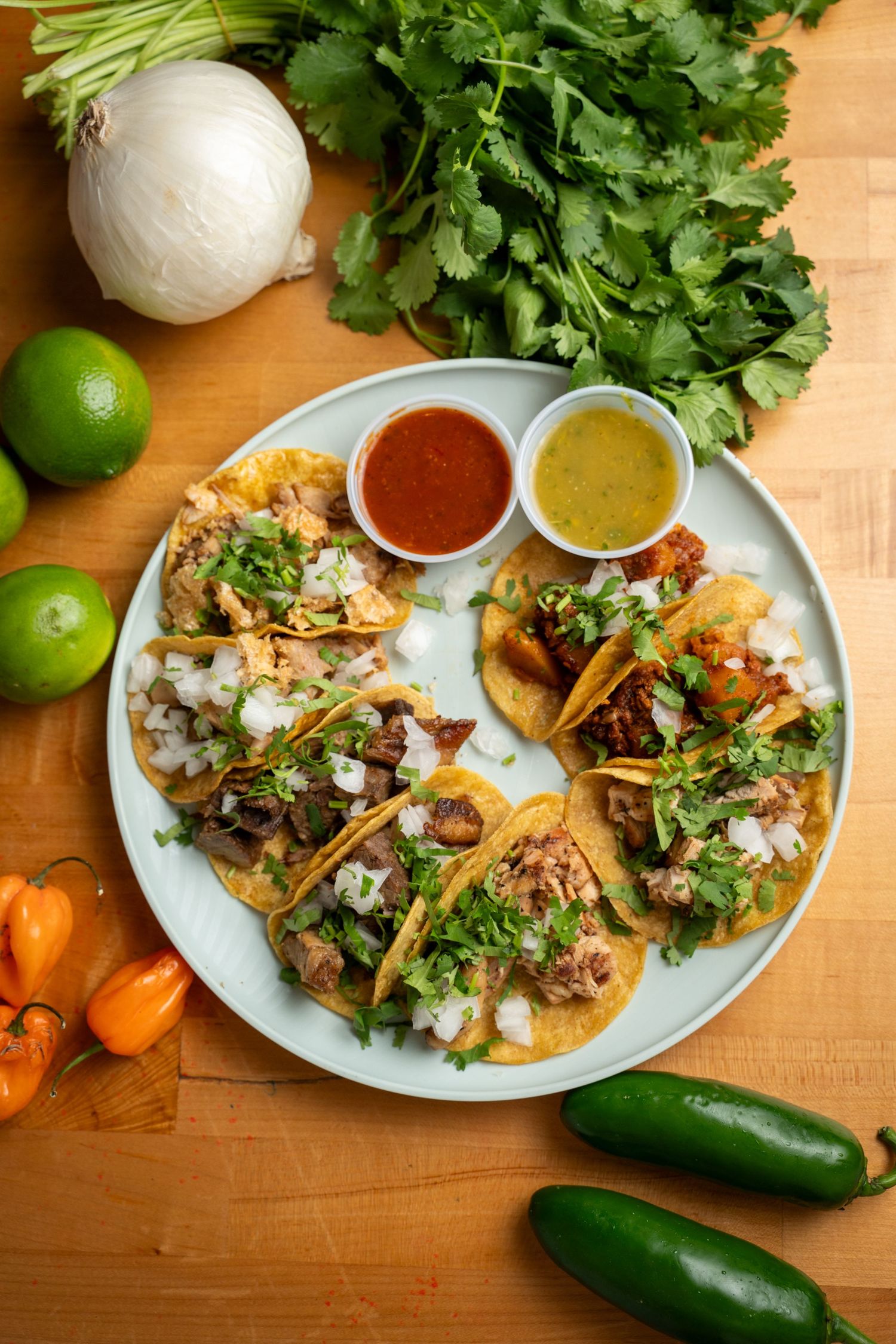 Mexican street tacos with fresh cilantro, onions, lime wedges and two types of salsa served on blue plates.