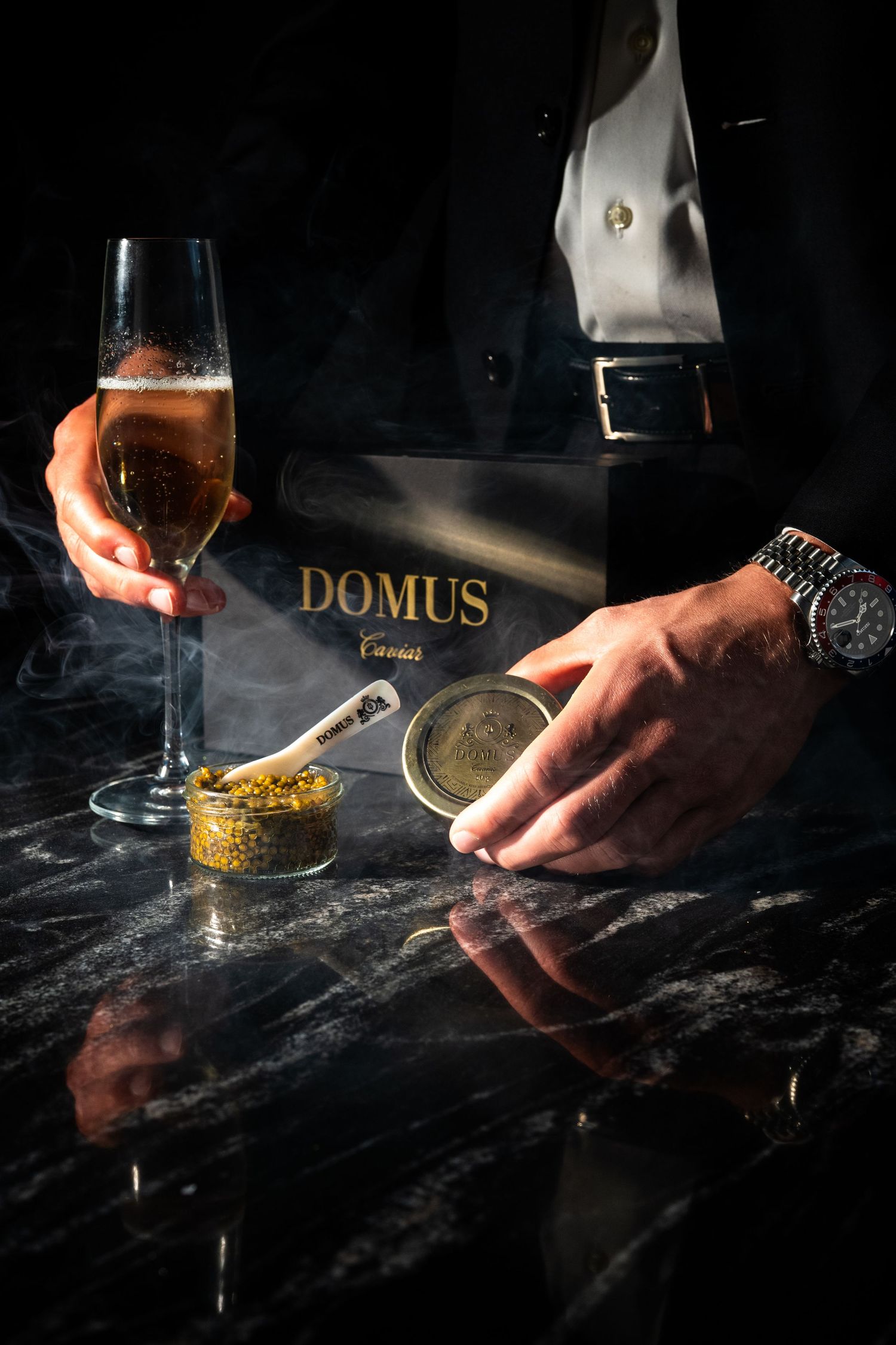 Man in suit opening Domus Caviar tin on marble surface with champagne flute and golden caviar spoon.