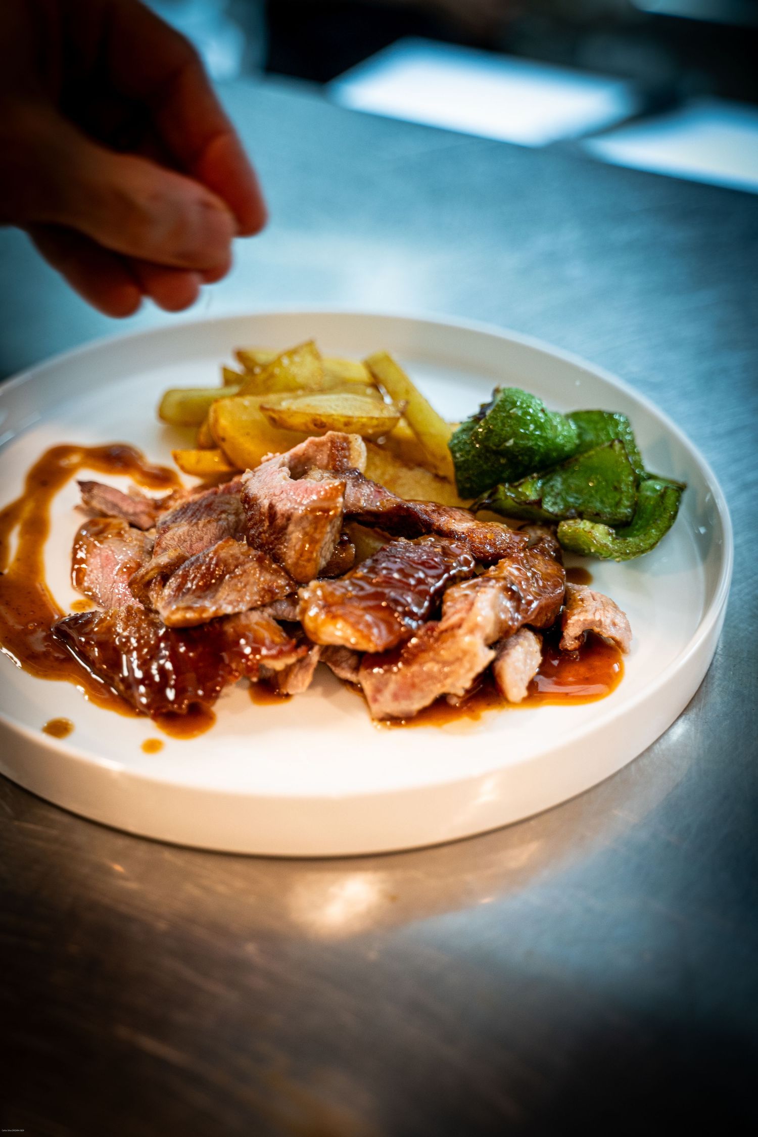 Sliced roasted meat with gravy served alongside crispy potatoes and steamed broccoli on a white plate.