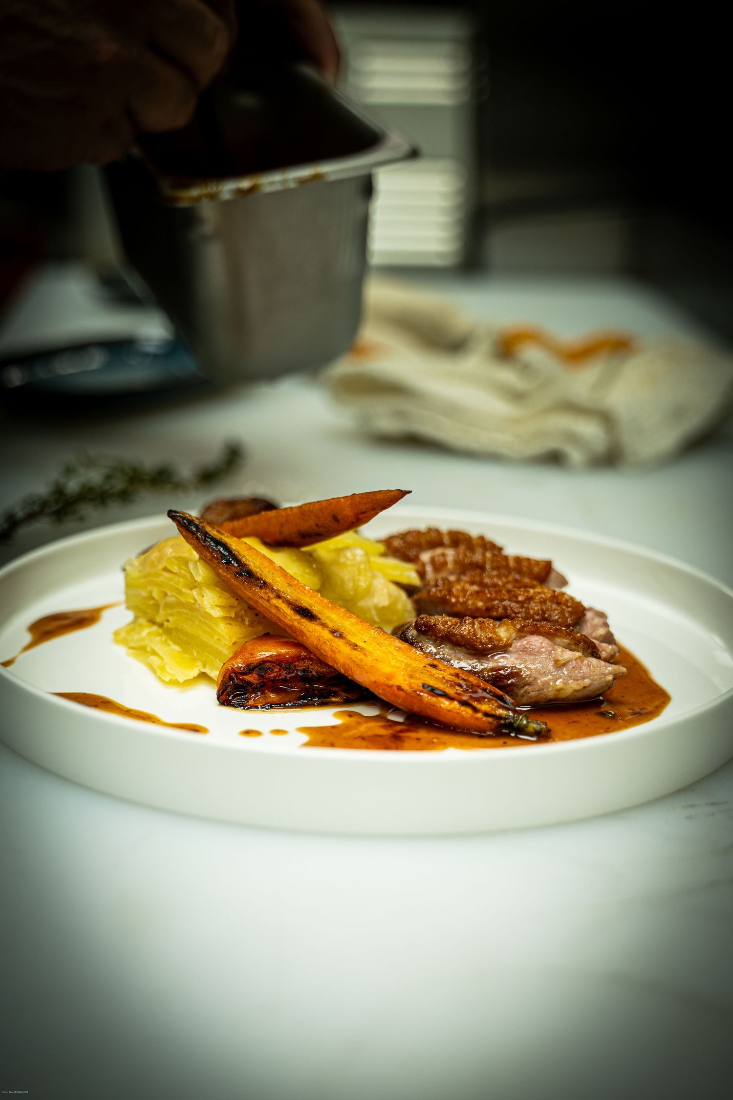 Elegant plated dish featuring sliced meat with roasted carrots and yellow garnish in a rich brown sauce on white plate.