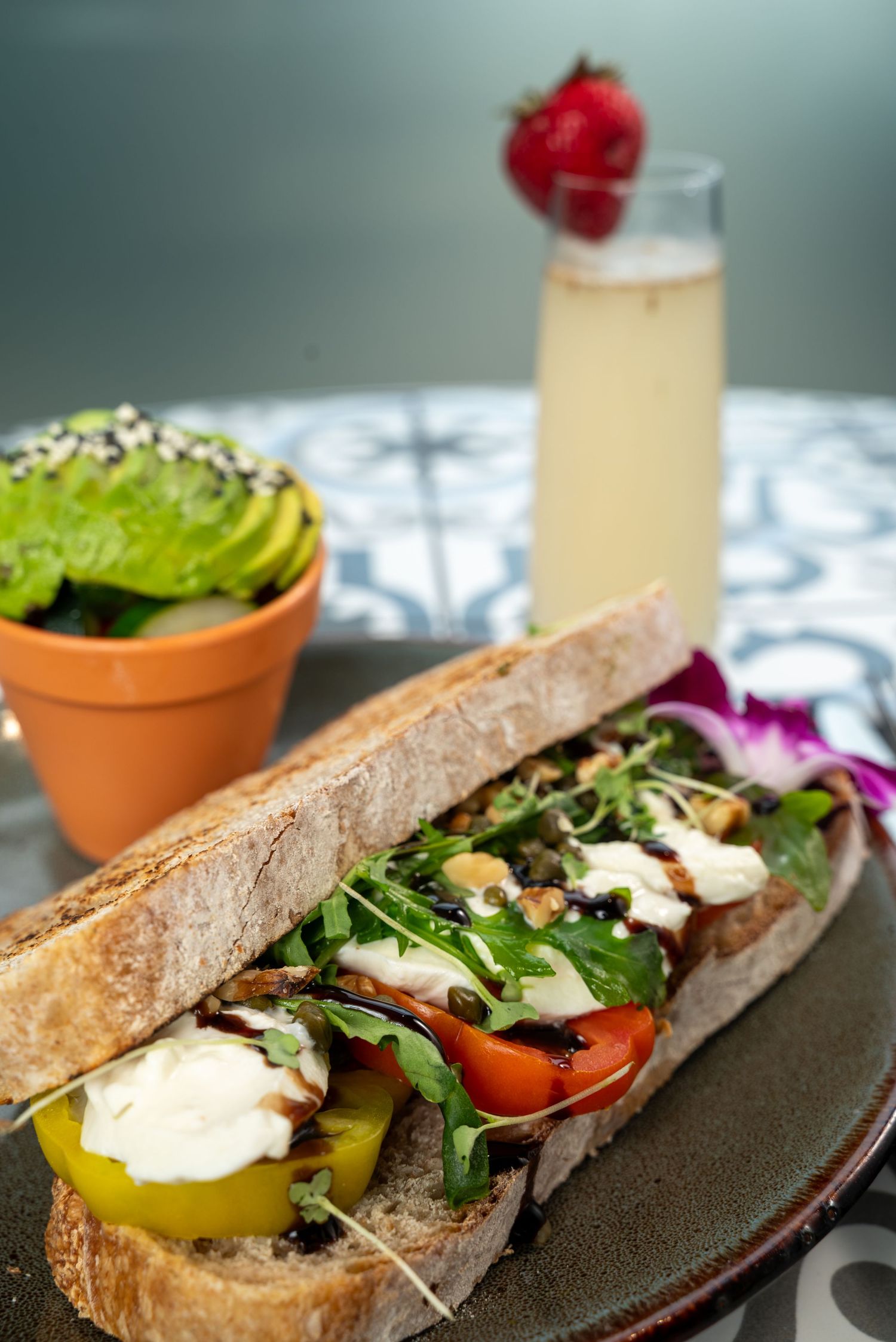 Fresh vegetable sandwich with avocado and sprouts served with citrus drink.