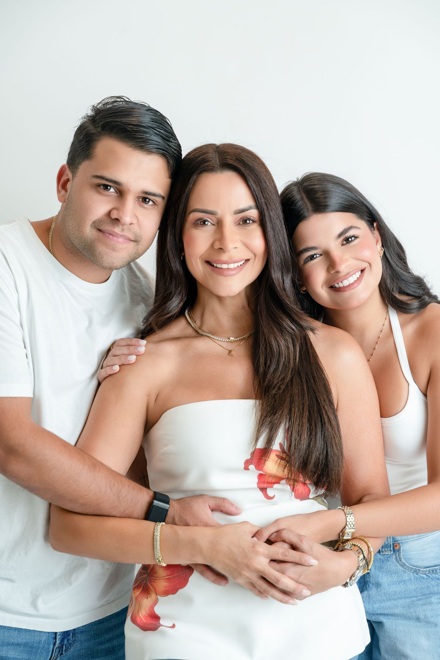 Three smiling friends pose together in white tops against a light background in a warm portrait photo.