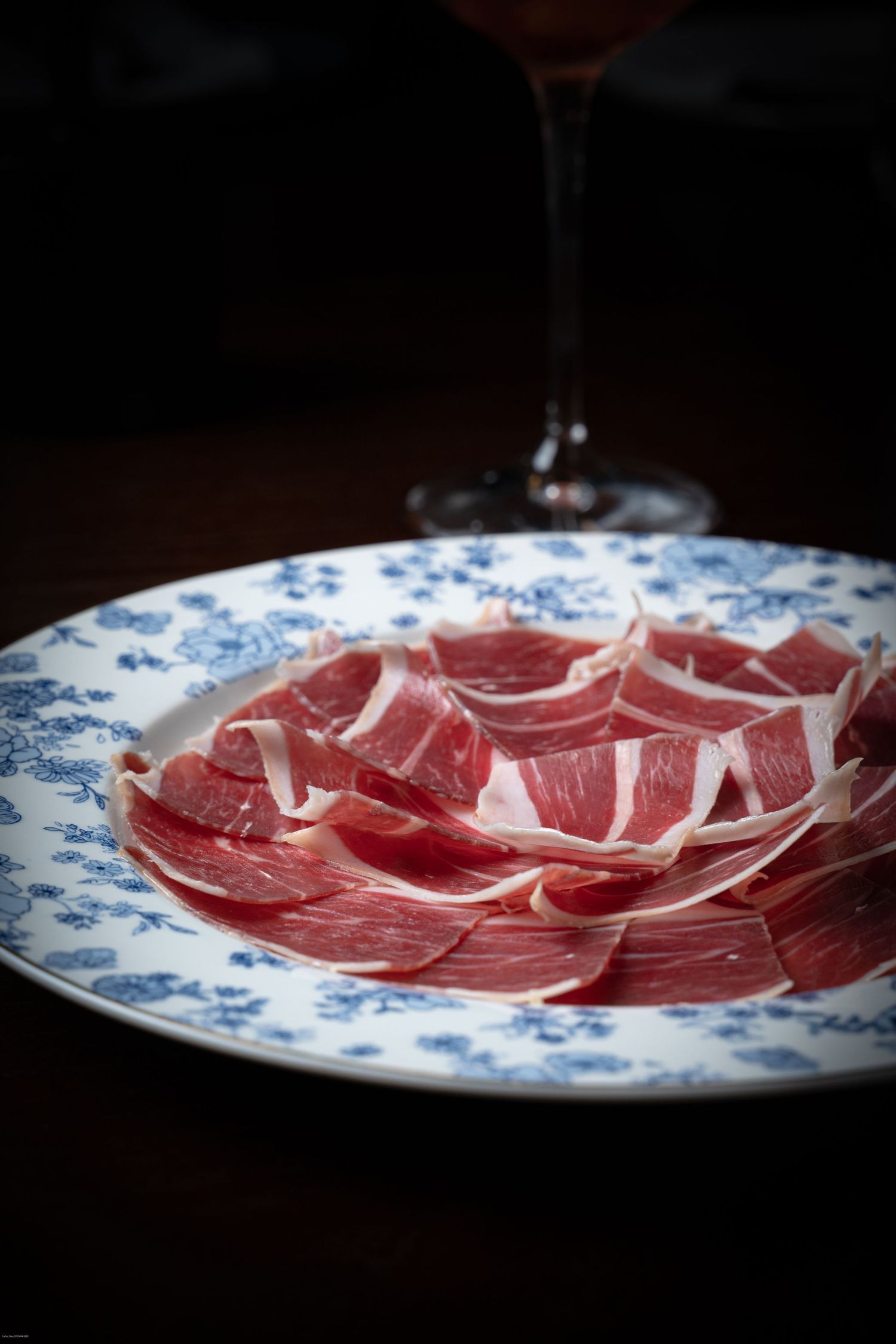 Thinly sliced prosciutto arranged on a blue and white floral pattern plate.