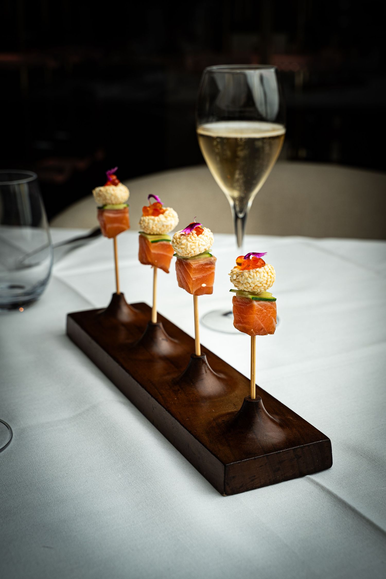 Salmon canapés on a wooden stand beside a glass of champagne at Cocody restaurant in Houston, Texas.