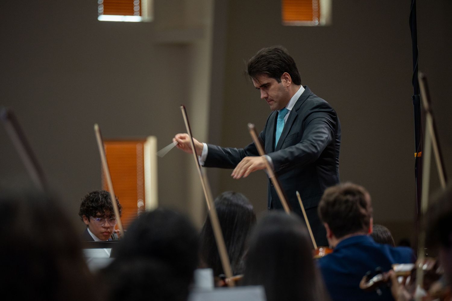 A conductor leads a classical music performance with an orchestra in a dimly lit concert hall.