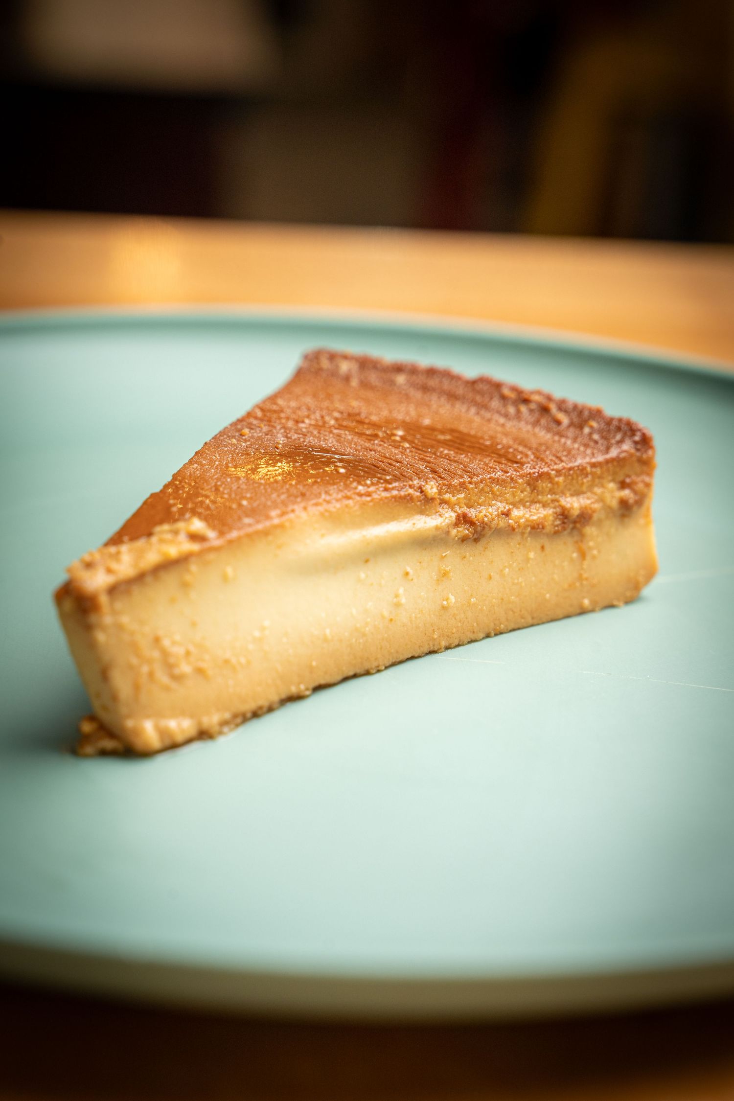 Close-up of a golden brown crème caramel dessert slice on a turquoise plate with smooth silky texture.