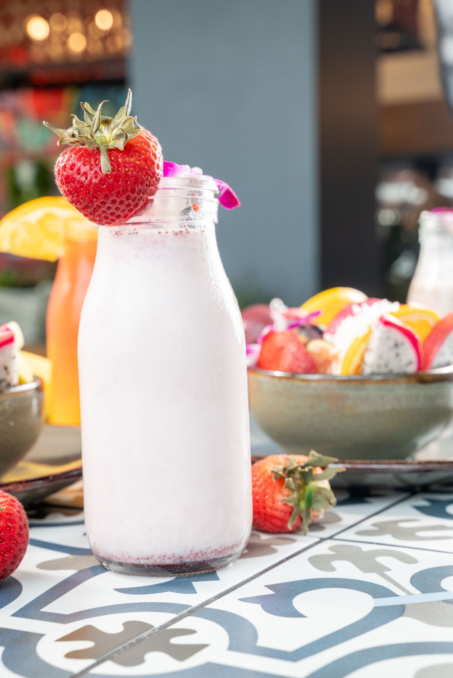 Pink smoothie in glass bottle topped with fresh strawberry on patterned tile surface.