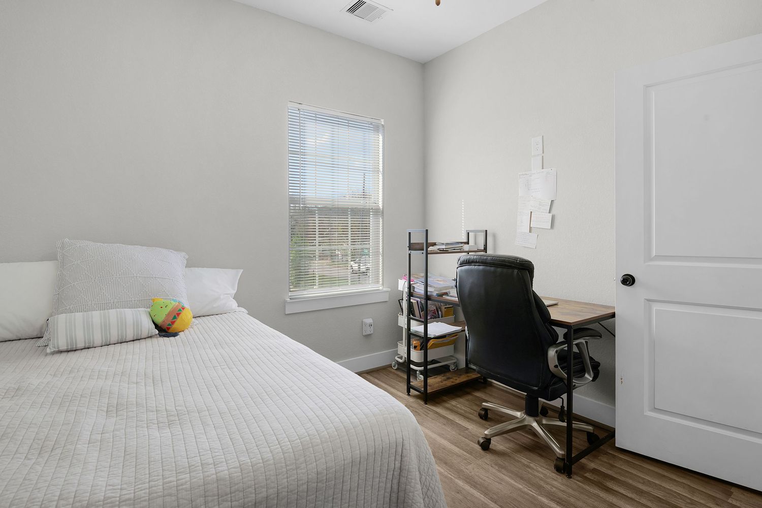 Minimalist bedroom with white bedding, wooden floors, and natural light streaming through windows.
