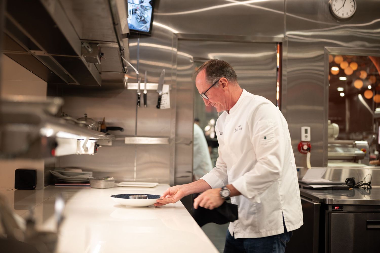 Chef in white coat carefully plates a dish in a modern professional restaurant kitchen.